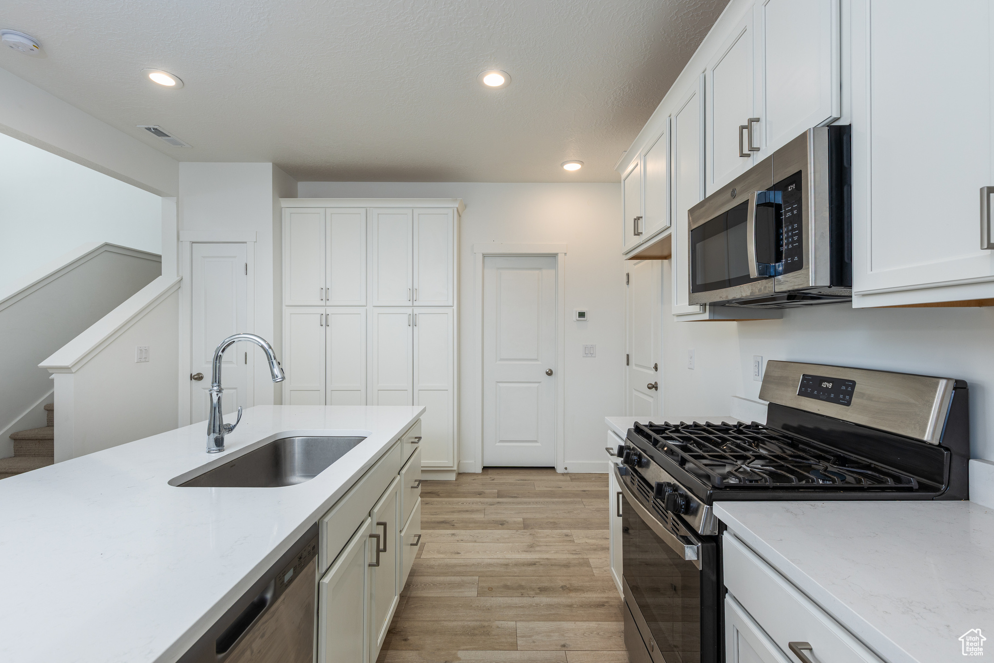 Kitchen featuring light wood-style flooring, appliances with stainless steel finishes, white cabinets, and a sink