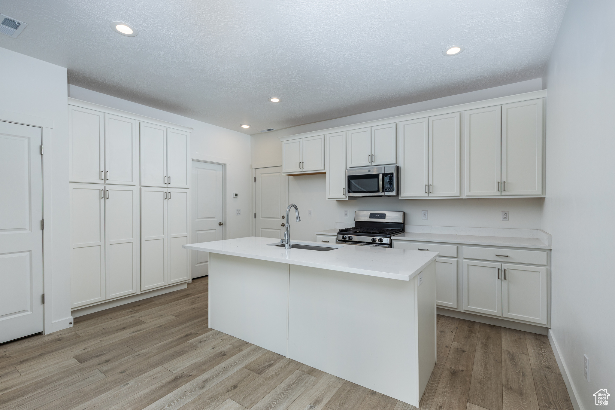 Kitchen featuring a kitchen island with sink, a sink, white cabinetry, light countertops, and appliances with stainless steel finishes