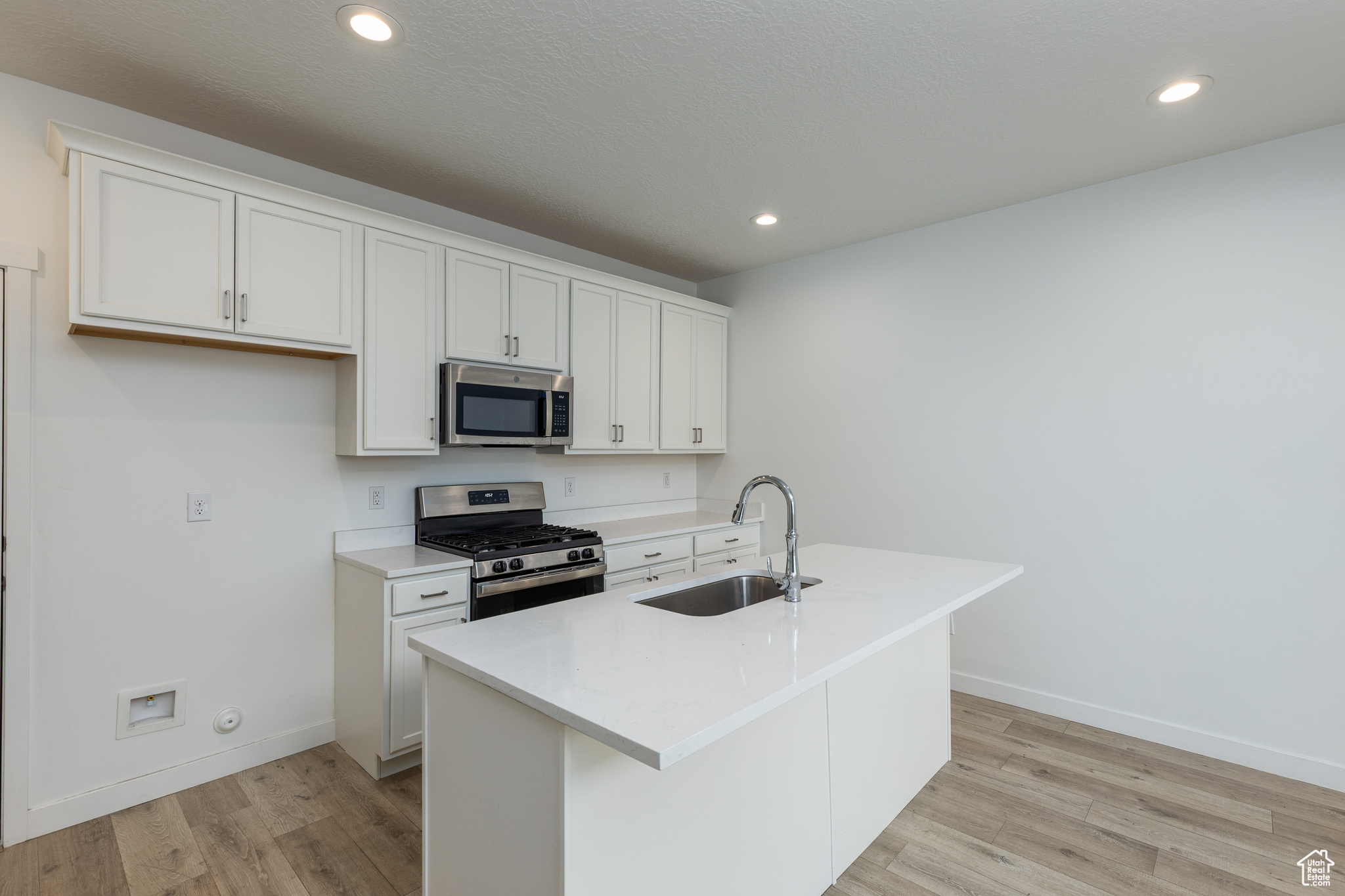 Kitchen with white cabinets, a kitchen island with sink, stainless steel appliances, and a sink