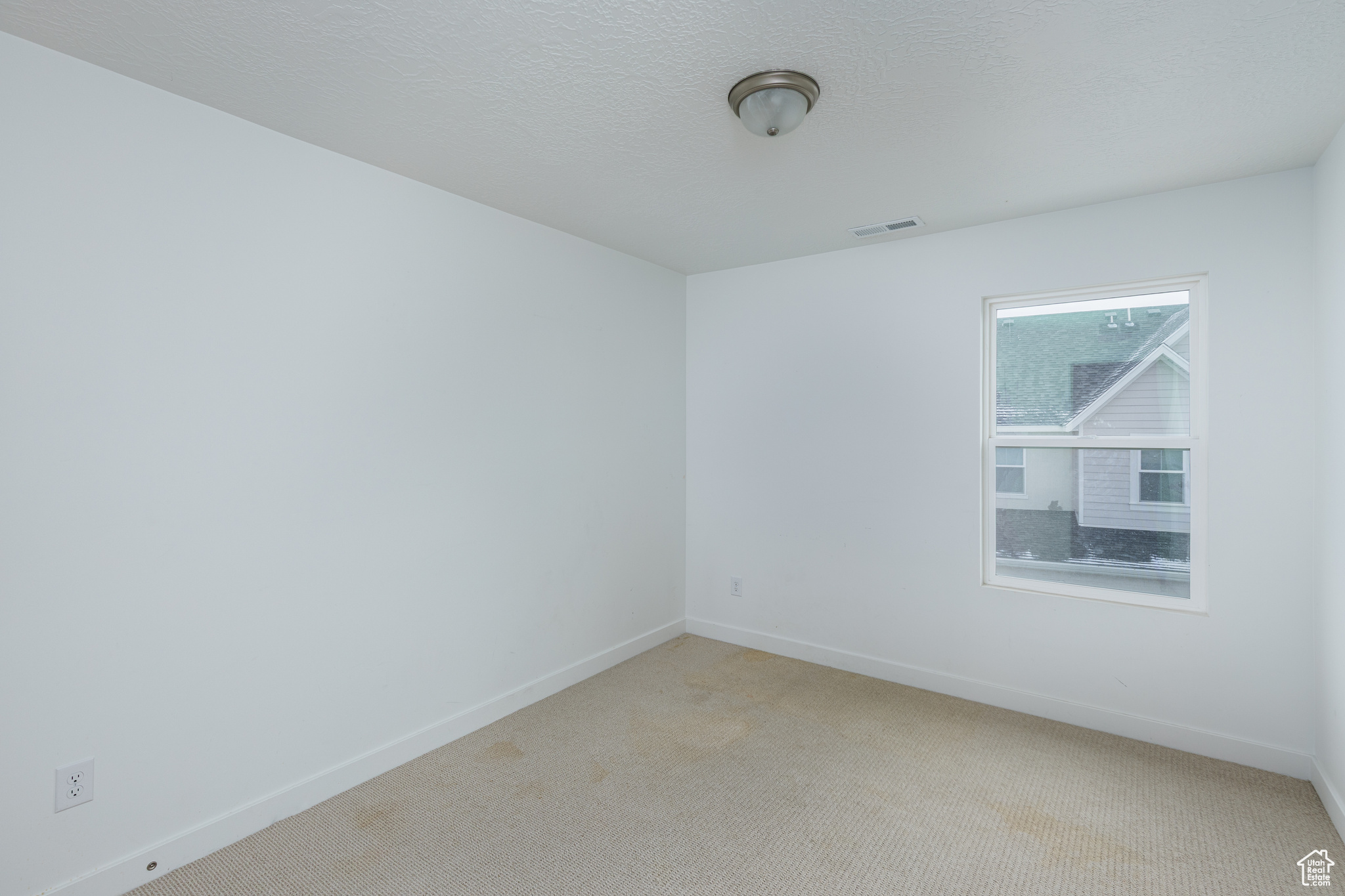 Spare room with baseboards, a textured ceiling, visible vents, and light colored carpet