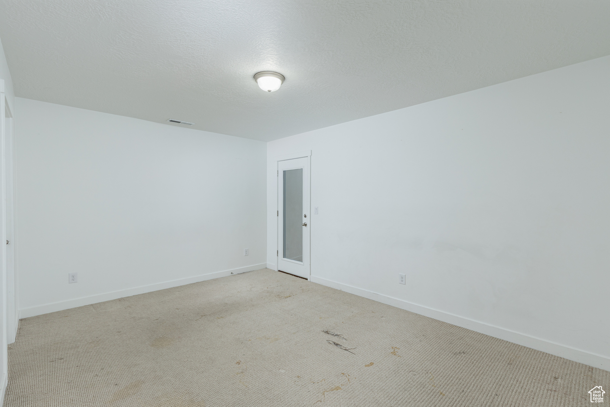 Spare room featuring visible vents, light carpet, baseboards, and a textured ceiling