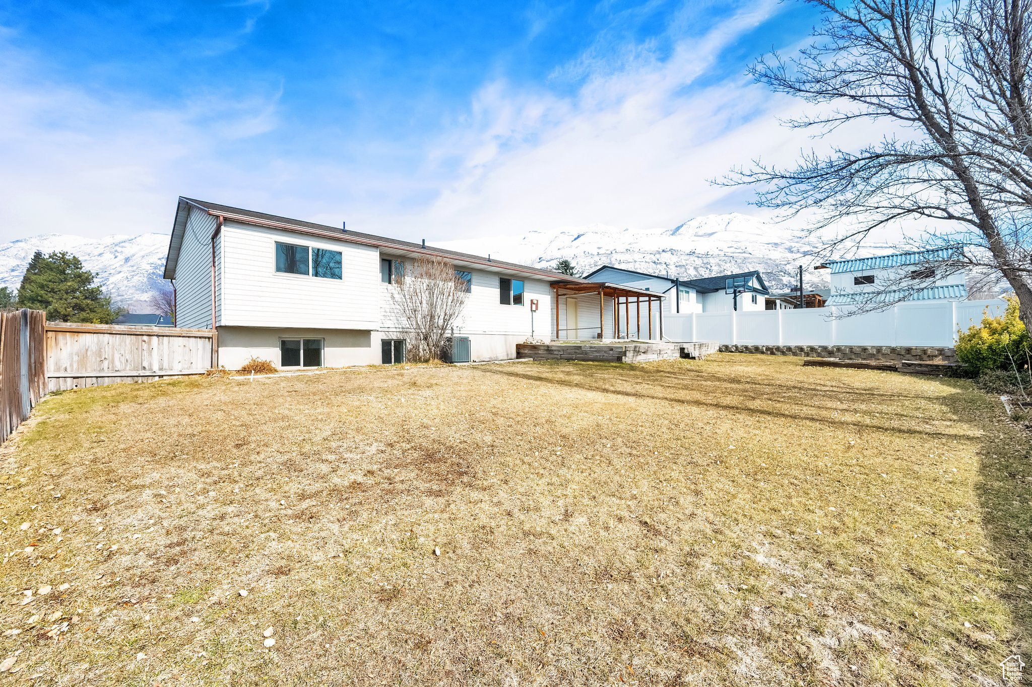 Back of house with central AC unit, a lawn, fence, and a mountain view