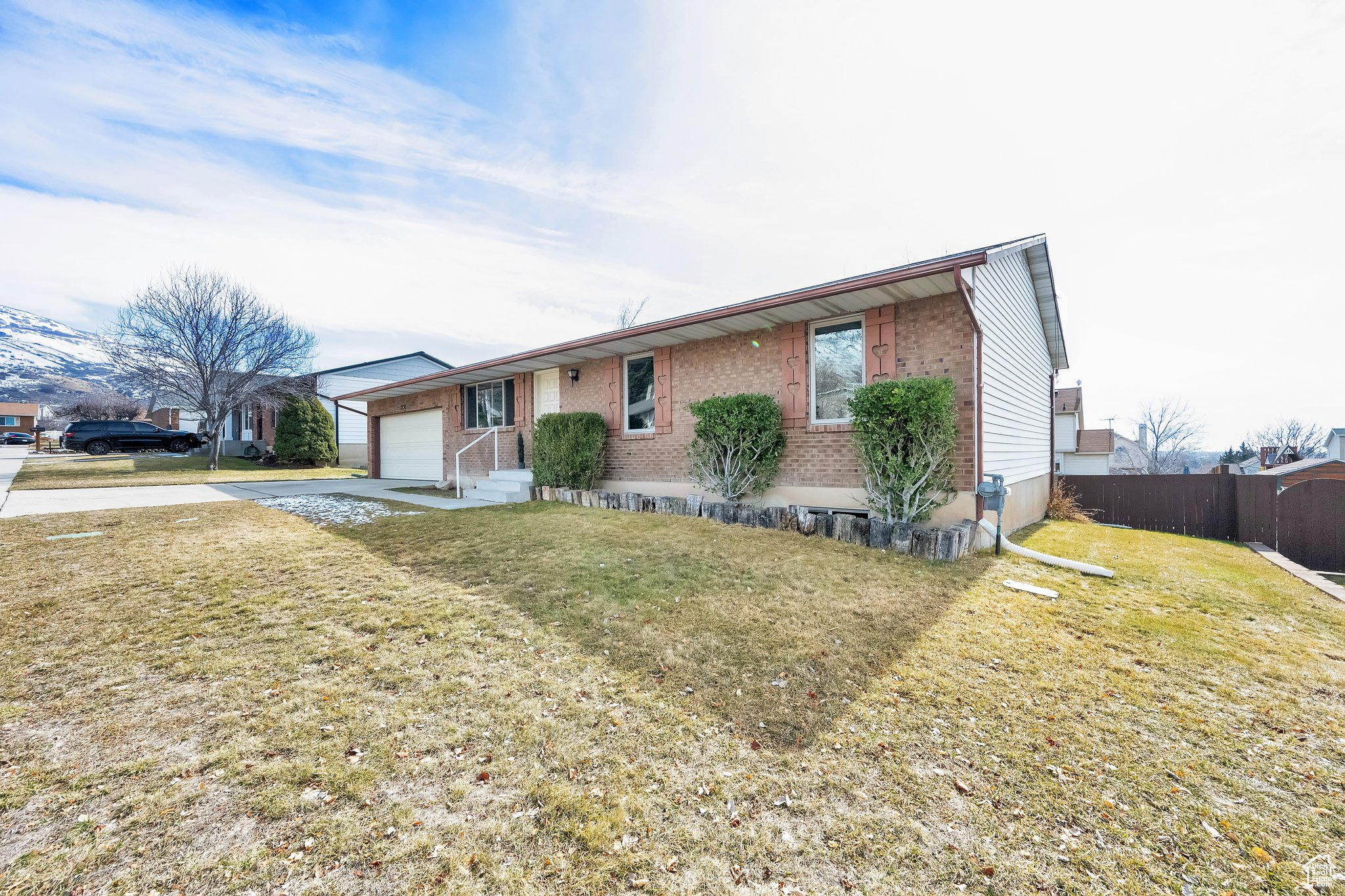 Single story home with brick siding, concrete driveway, fence, a garage, and a front lawn