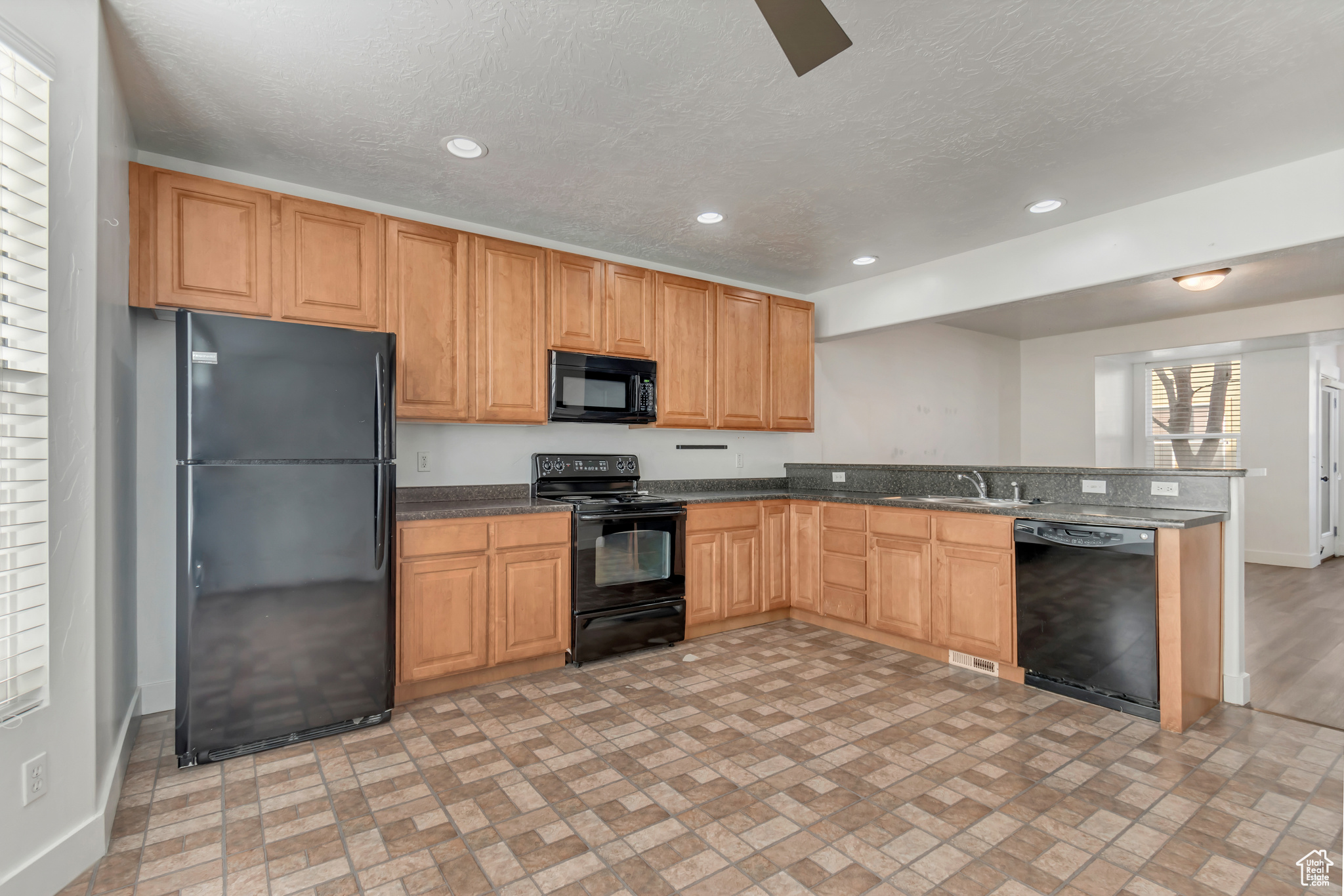 Kitchen featuring baseboards, a textured ceiling, black appliances, a sink, and recessed lighting