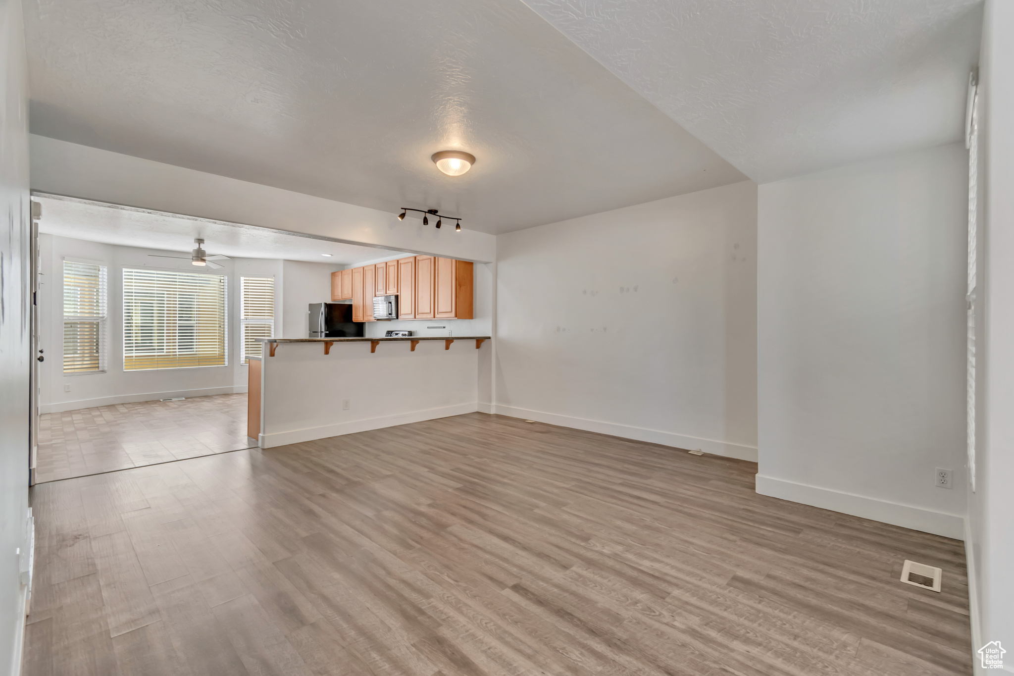 Unfurnished living room featuring a ceiling fan, visible vents, light wood-style flooring, and baseboards