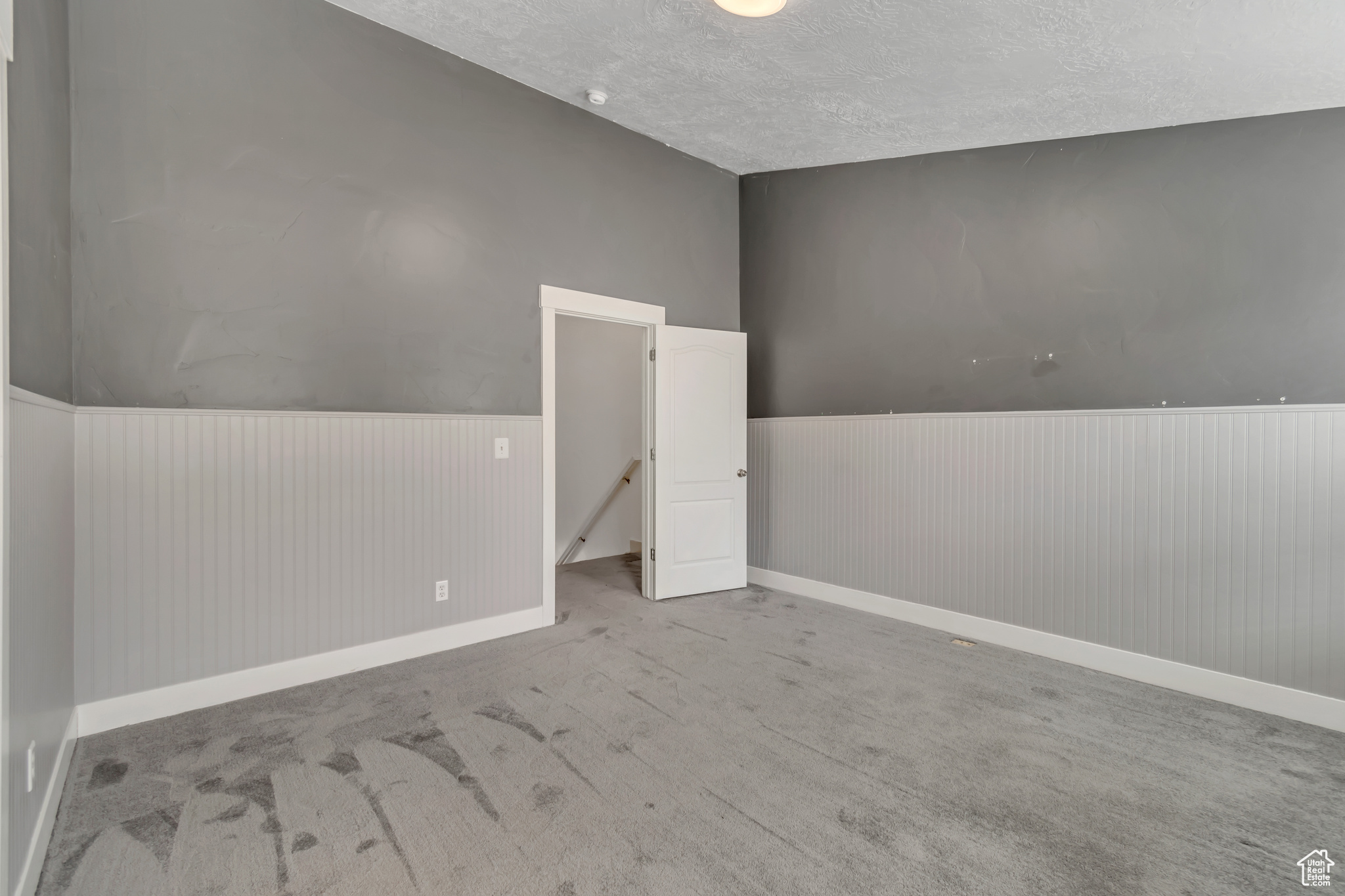 Unfurnished room featuring light colored carpet, a textured ceiling, and wainscoting