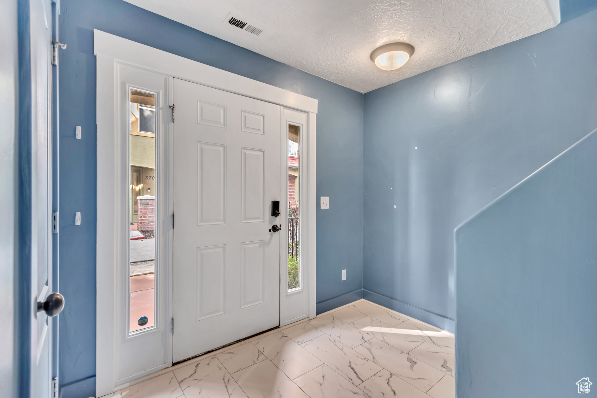 Foyer with marble finish floor, visible vents, and a textured ceiling