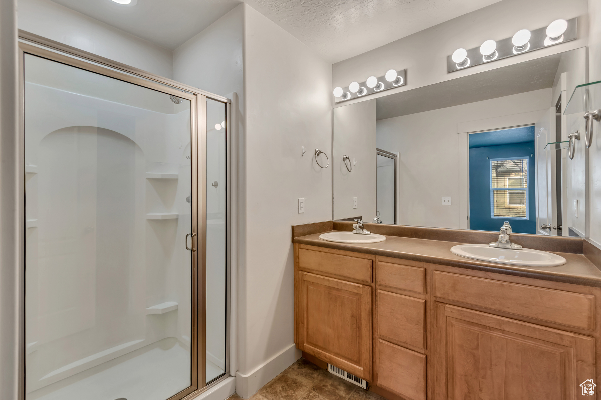 Full bath featuring visible vents, a sink, a shower stall, and double vanity