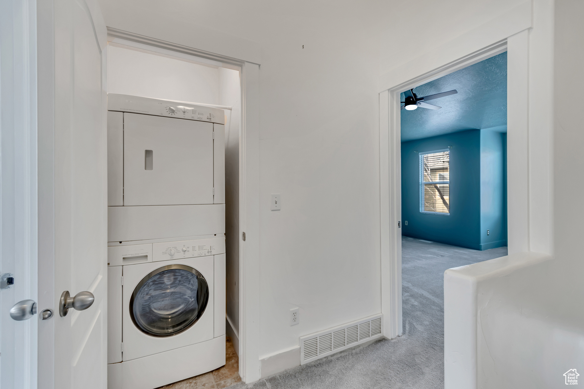 Clothes washing area featuring light colored carpet, visible vents, stacked washer / dryer, laundry area, and baseboards