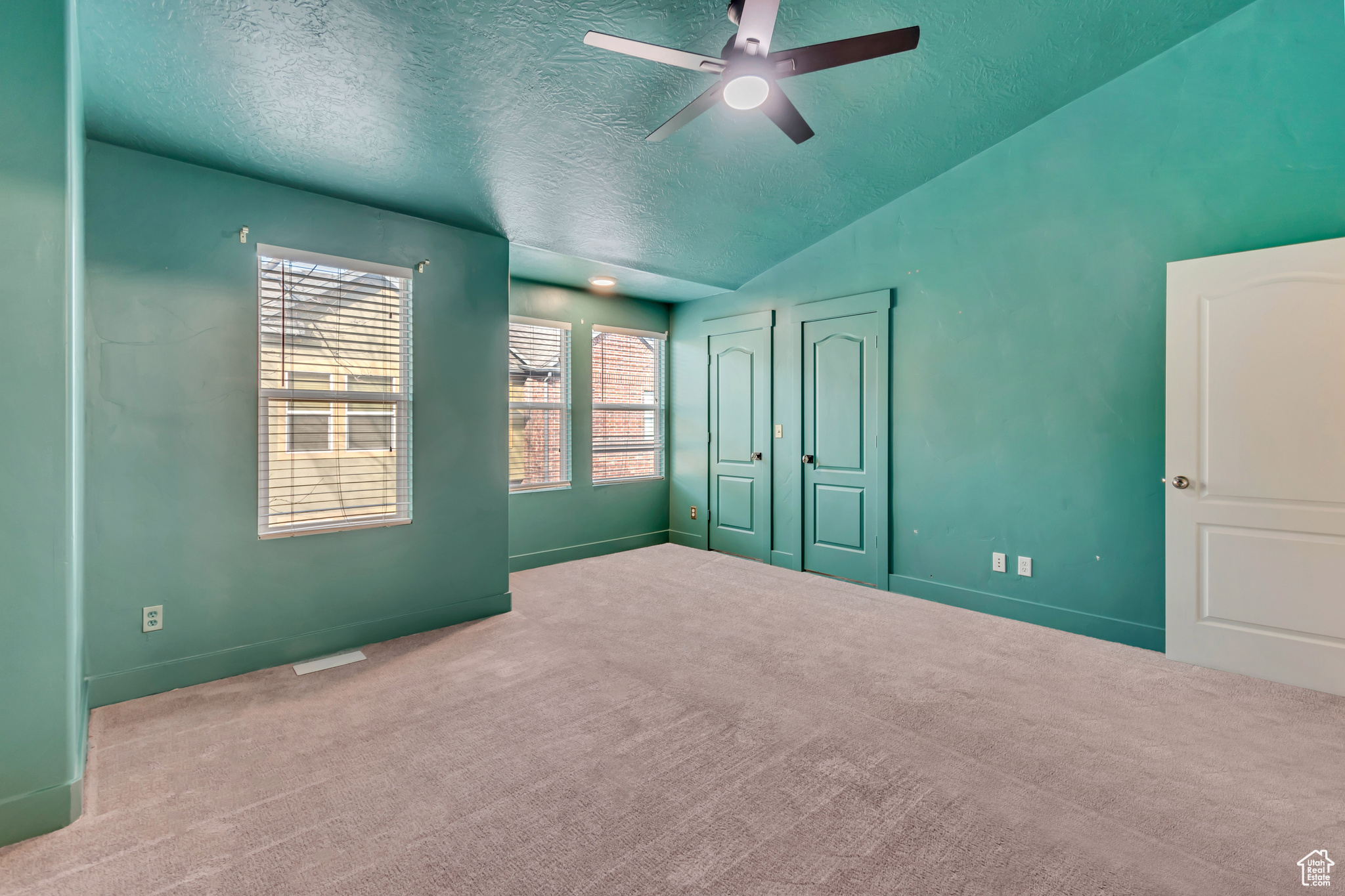 Empty room with light carpet, baseboards, a ceiling fan, lofted ceiling, and a textured ceiling