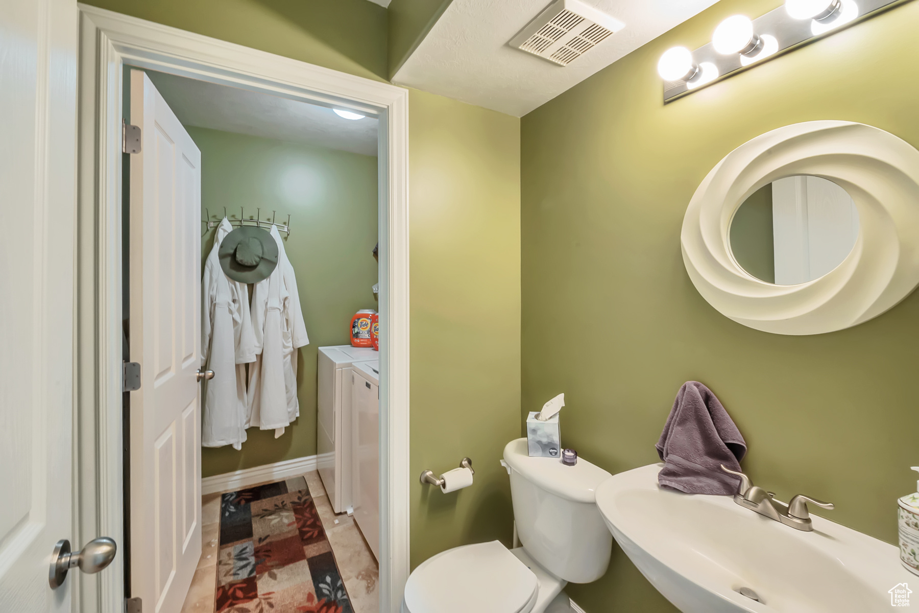 Half bathroom featuring toilet, a sink, visible vents, and washer and dryer