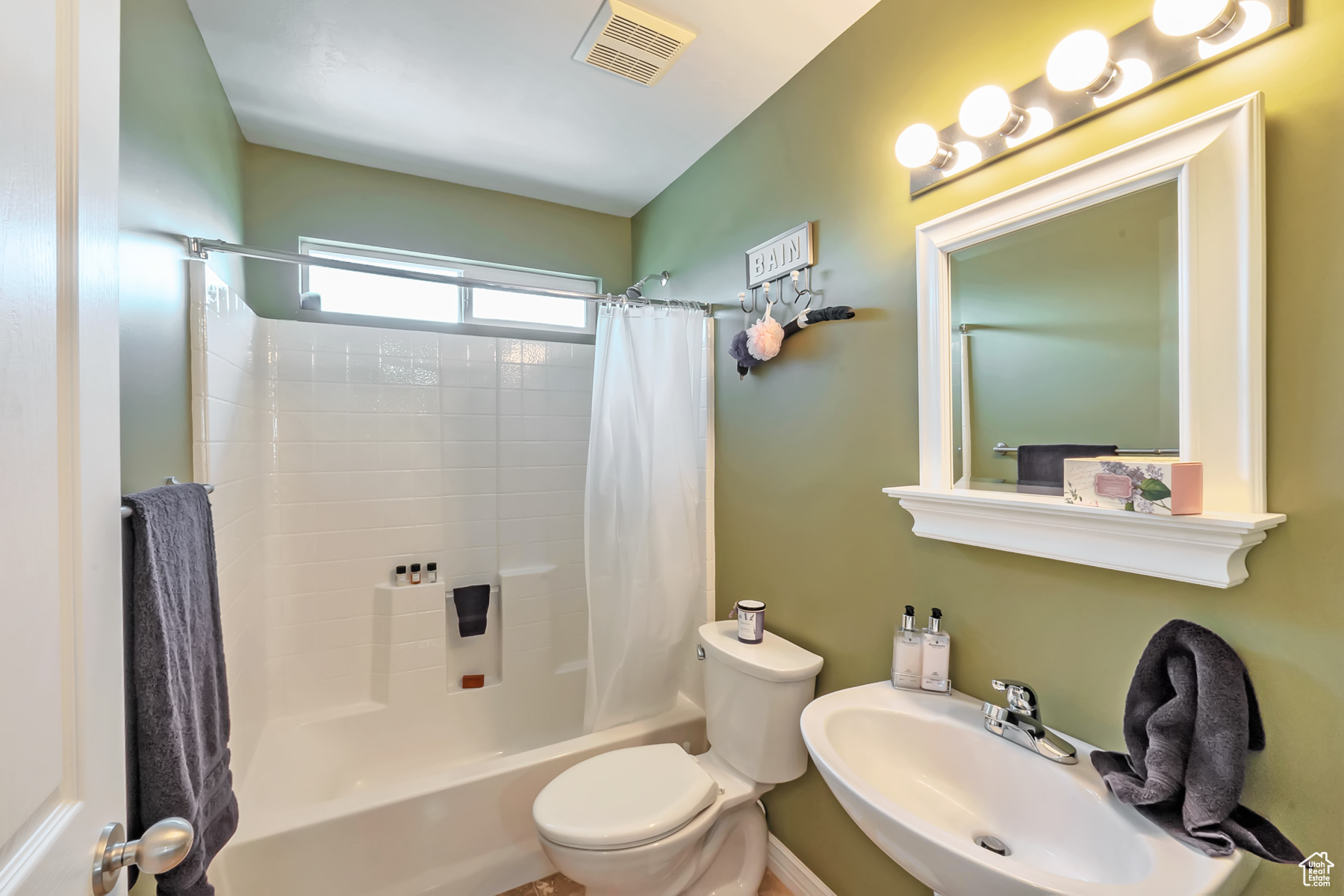 Bathroom featuring toilet, shower / bath combo, visible vents, and a sink