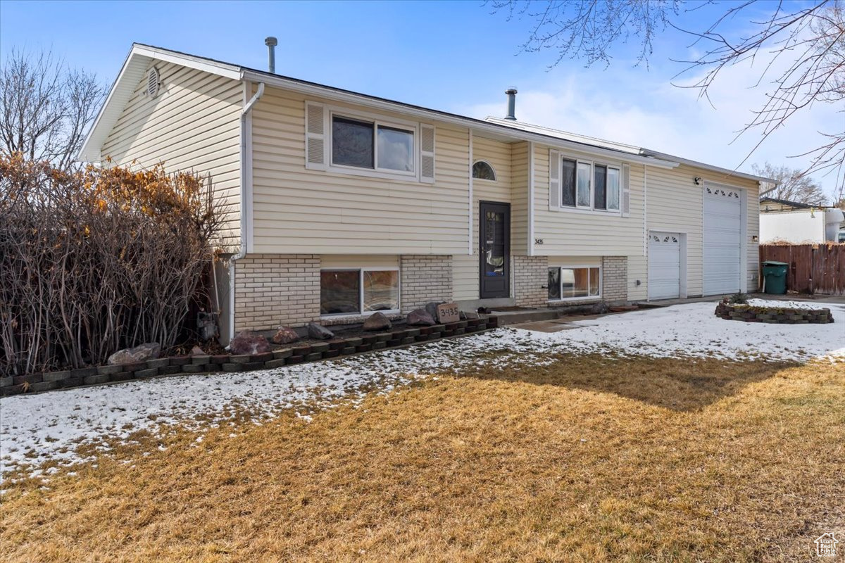 Bi-level home featuring a garage, brick siding, and a lawn