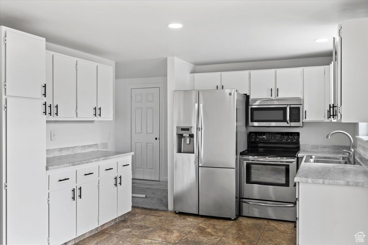 Kitchen featuring stone finish floor, appliances with stainless steel finishes, light countertops, white cabinetry, and a sink