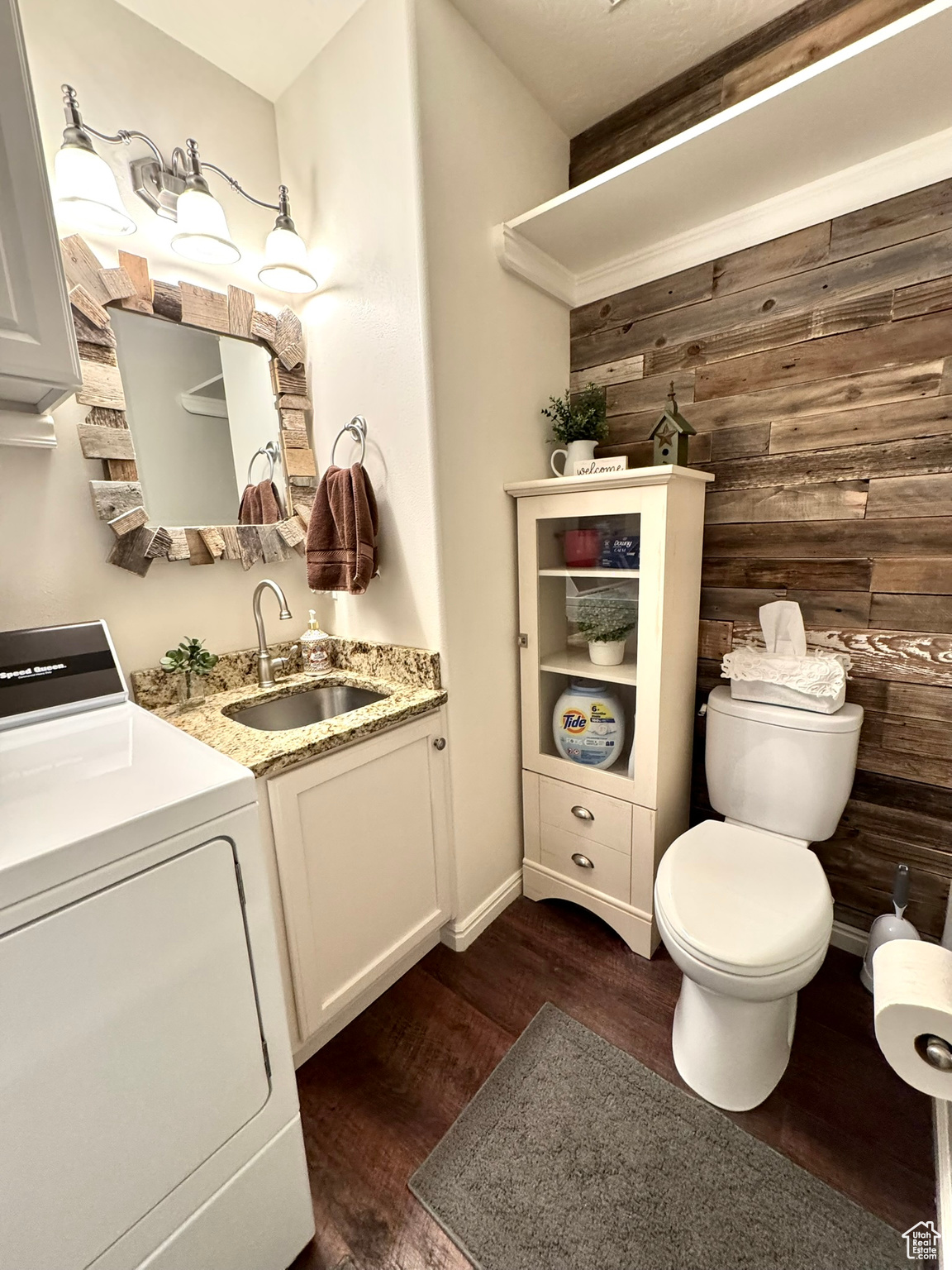 Bathroom featuring washer / dryer, toilet, wood finished floors, vanity, and wood walls