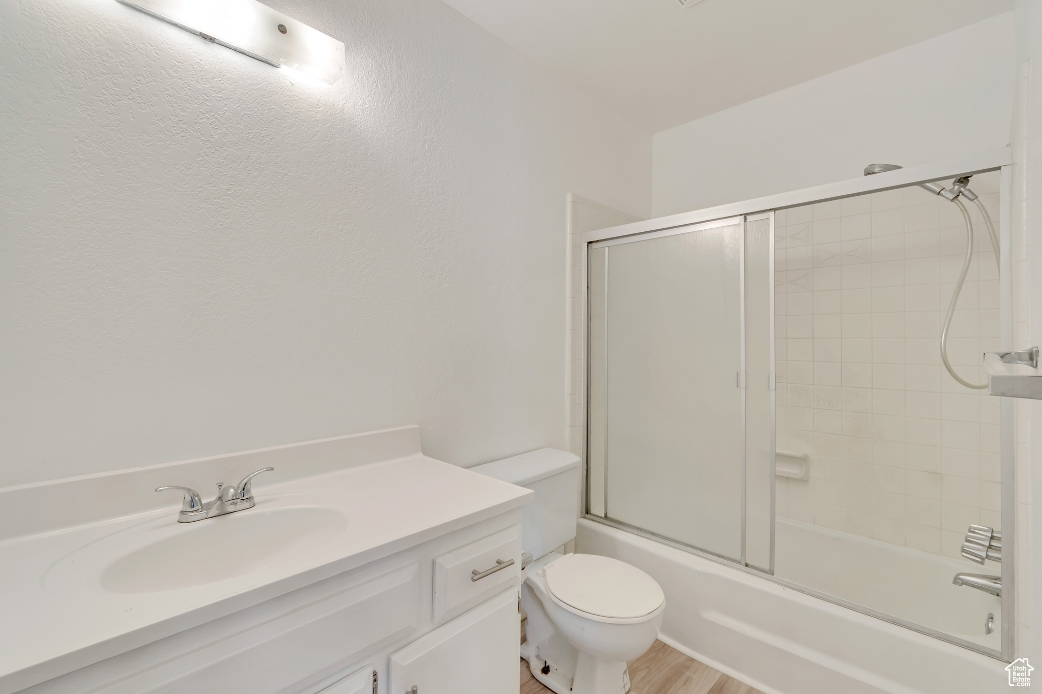 Bathroom with toilet, shower / bath combination with glass door, wood finished floors, and vanity