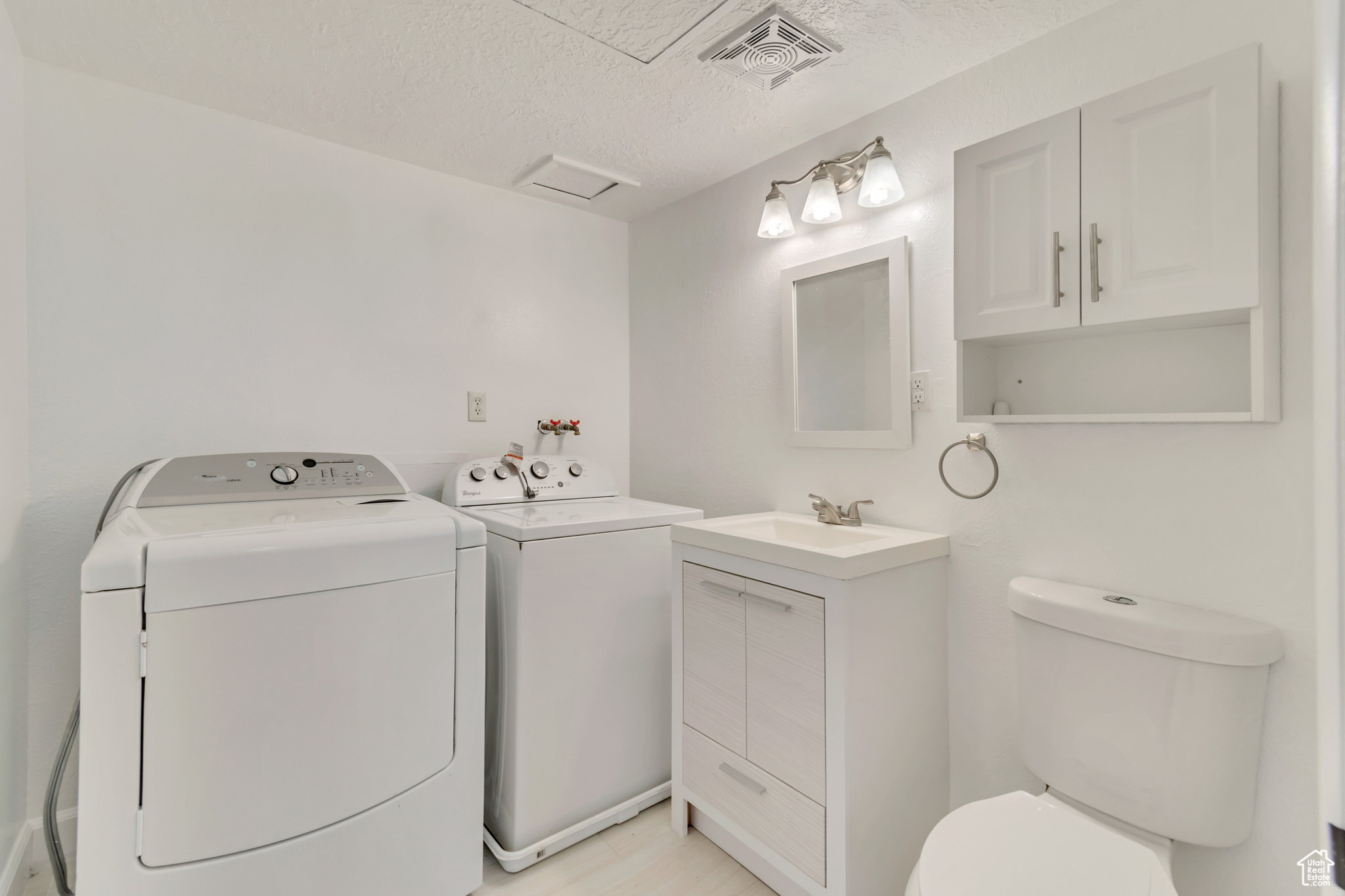 Laundry room featuring a textured ceiling, laundry area, separate washer and dryer, a sink, and visible vents