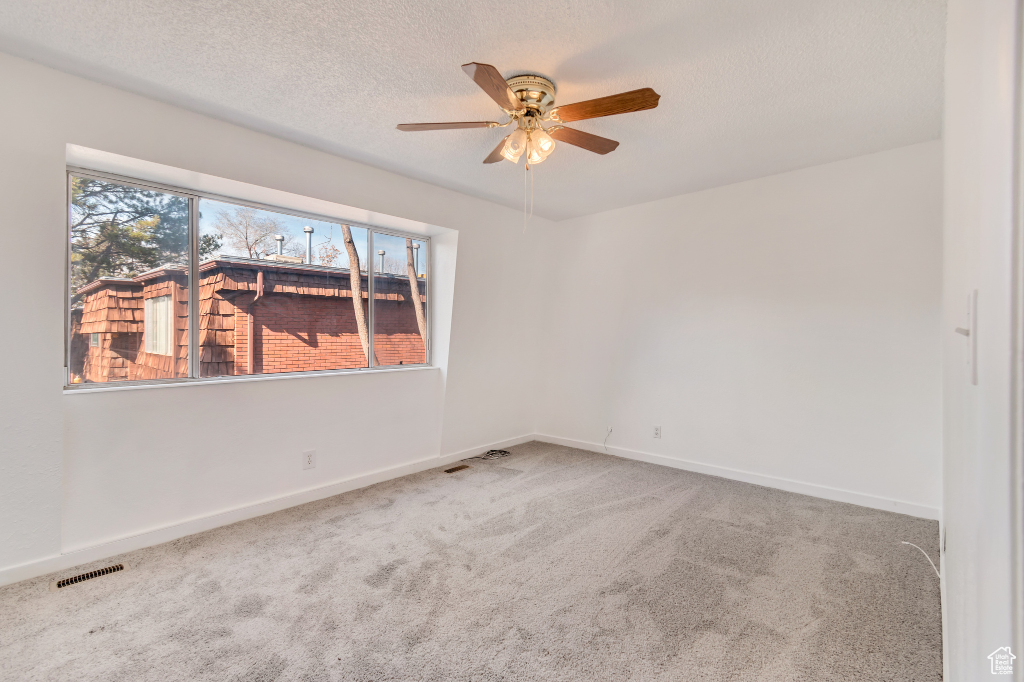 Carpeted empty room featuring a ceiling fan, baseboards, visible vents, and a textured ceiling