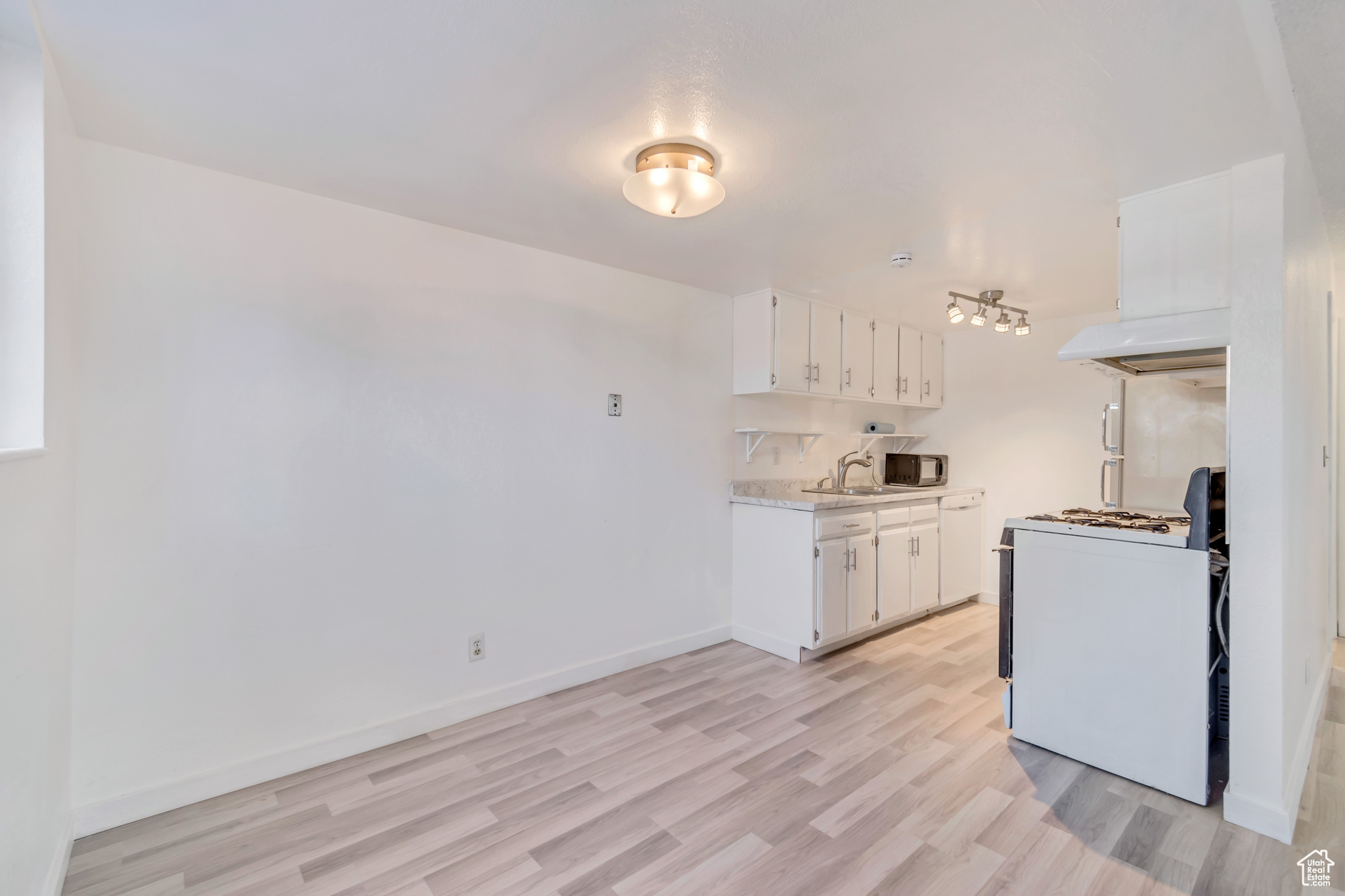 Kitchen with white cabinets, light countertops, light wood-type flooring, range hood, and white stove