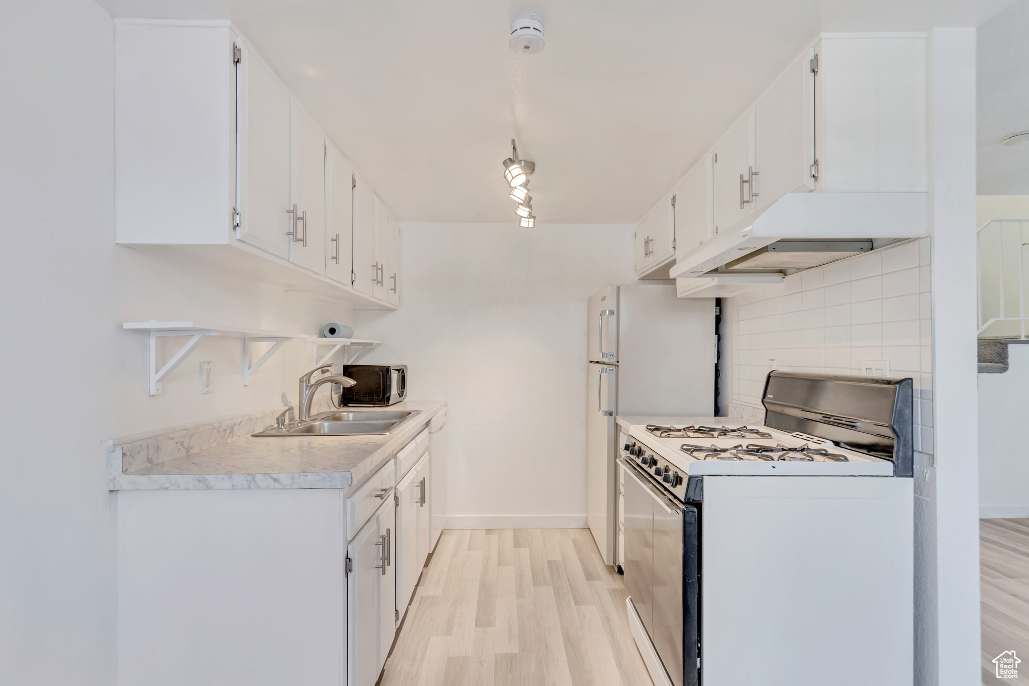 Kitchen with light wood finished floors, white gas range, light countertops, white cabinetry, and under cabinet range hood