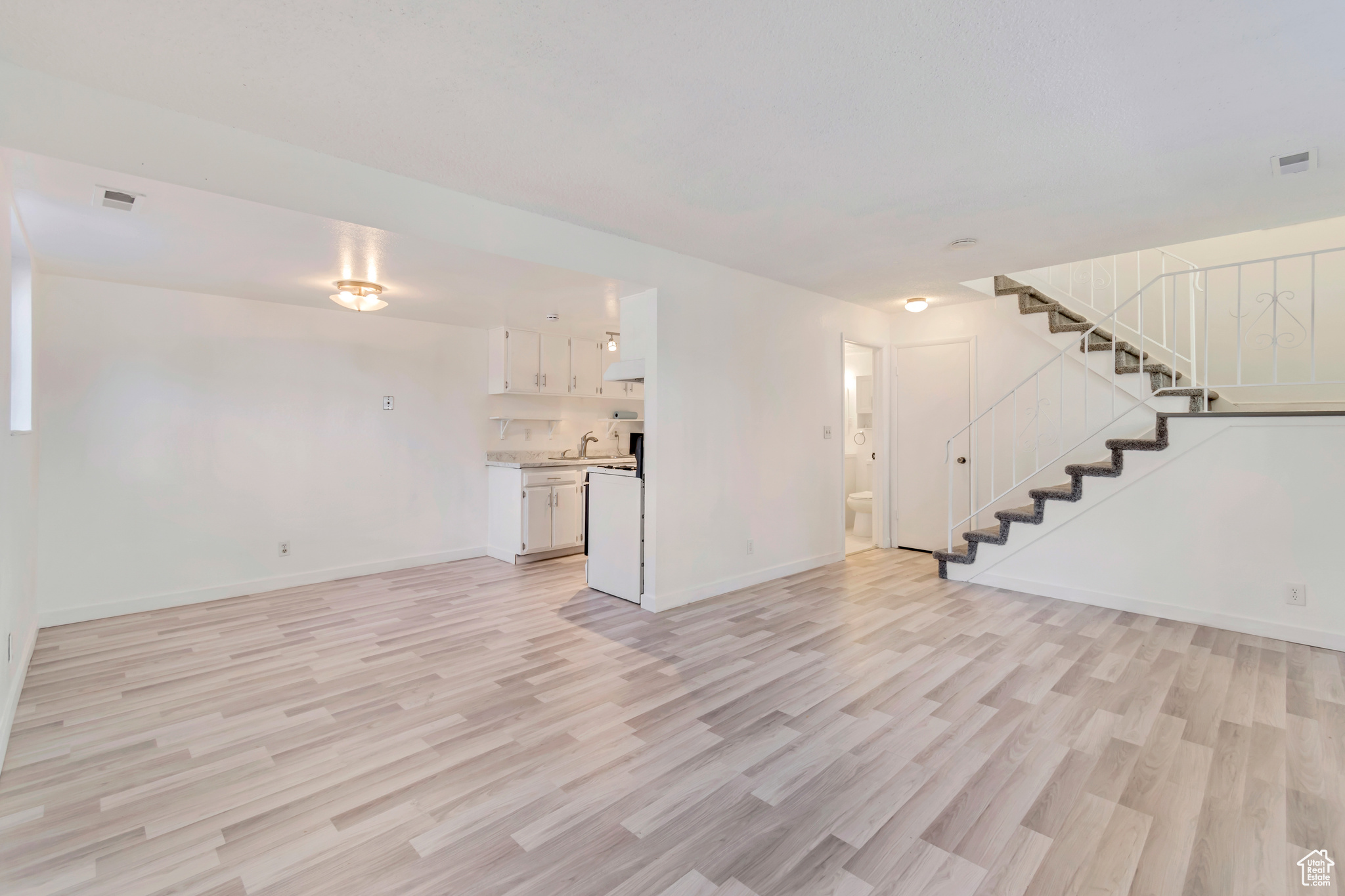 Unfurnished living room with visible vents, stairway, a sink, light wood-type flooring, and baseboards