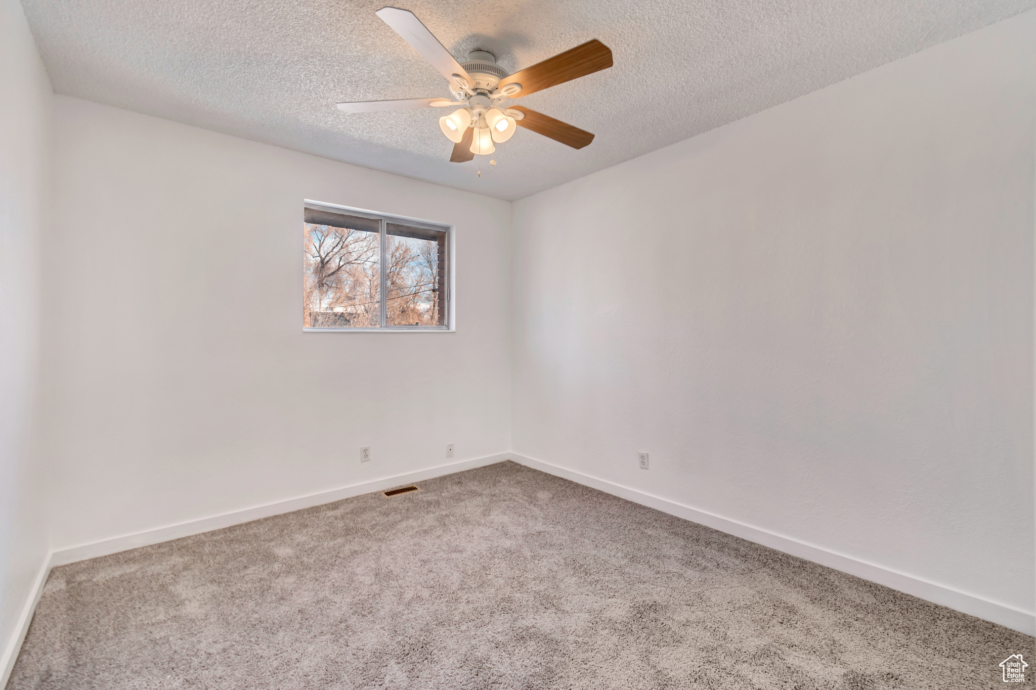 Carpeted empty room featuring a textured ceiling, visible vents, a ceiling fan, and baseboards