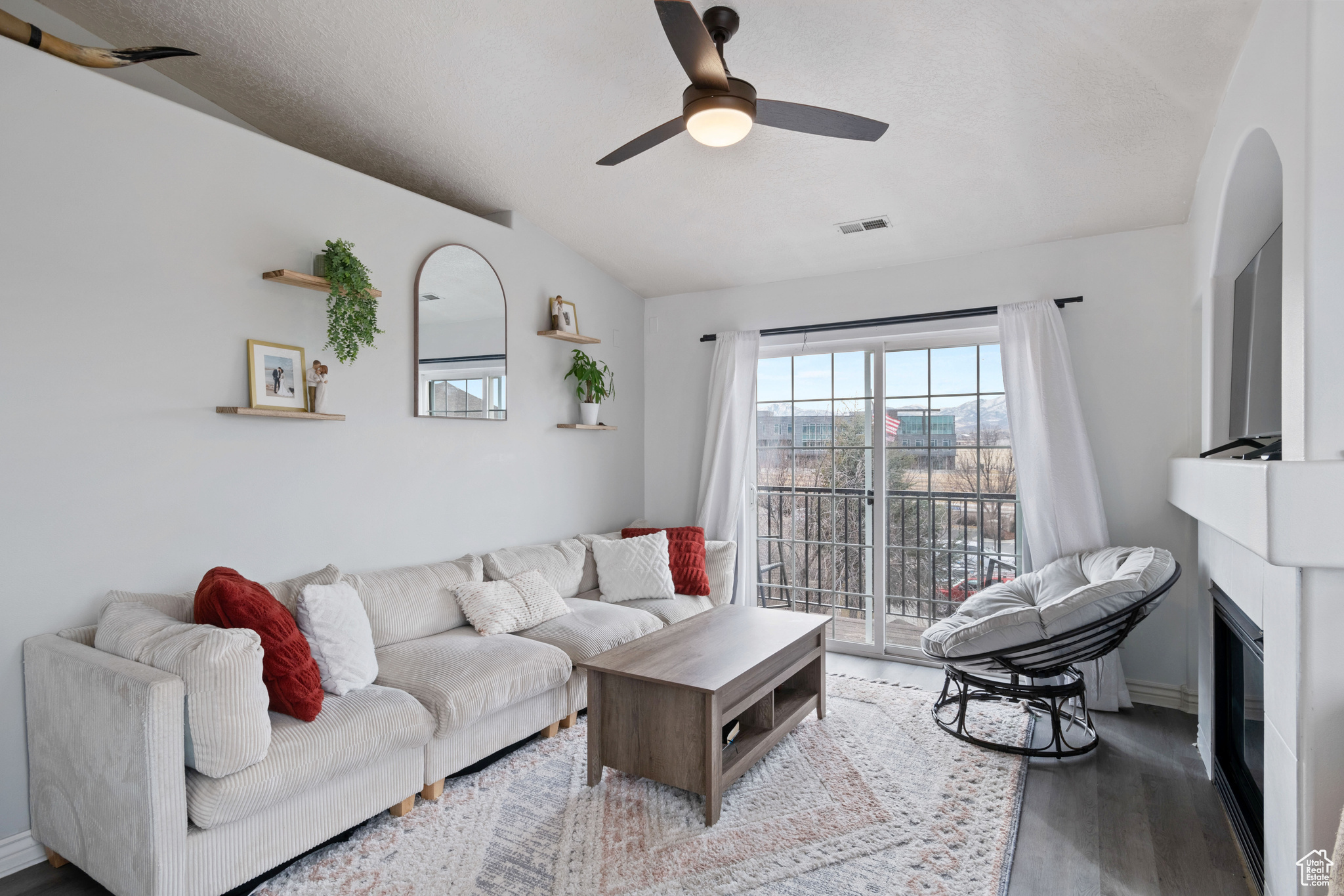 Living area featuring a ceiling fan, a glass covered fireplace, visible vents, and wood finished floors