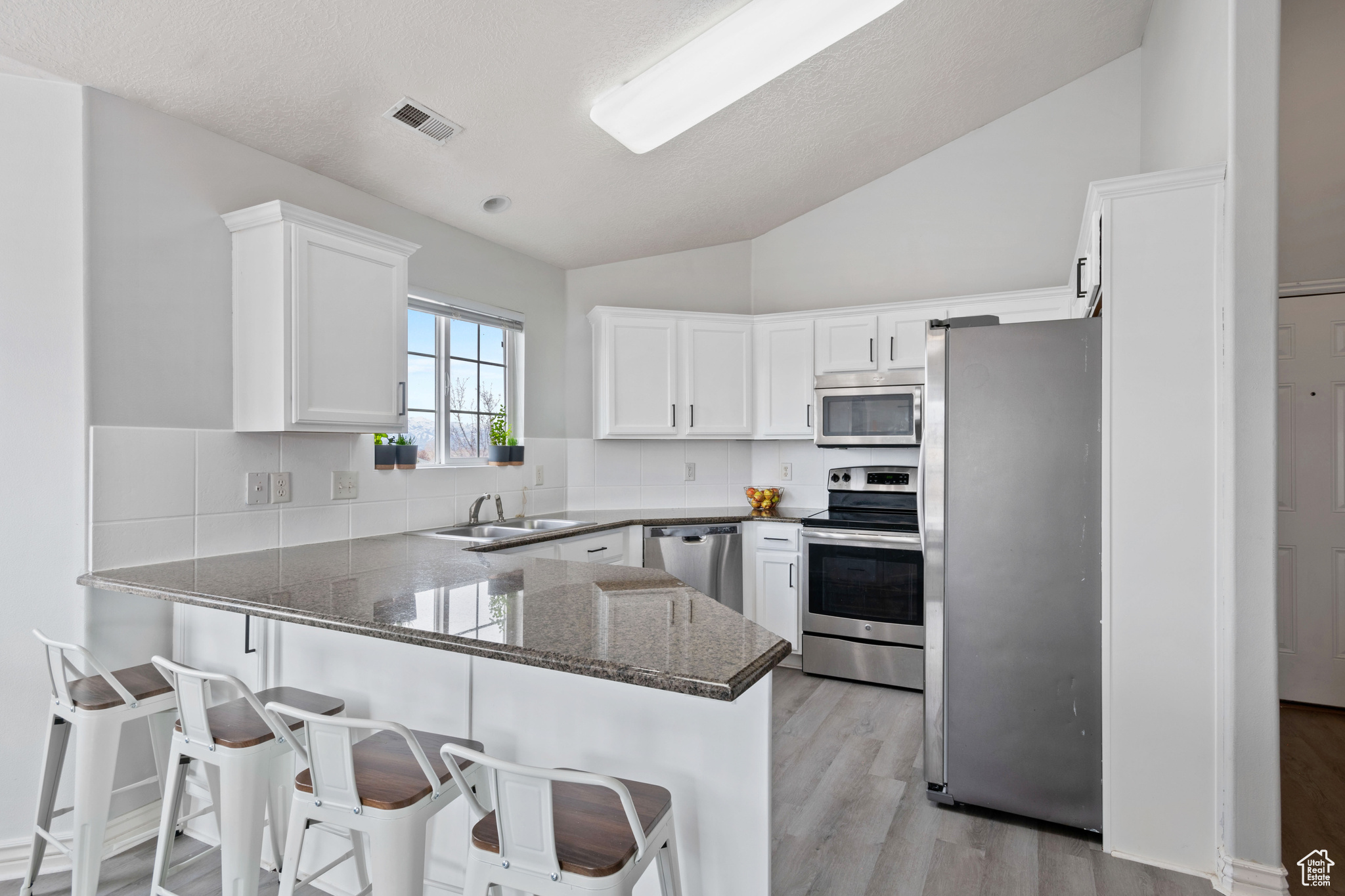 Kitchen featuring stainless steel appliances, white cabinets, a sink, a peninsula, and a kitchen bar