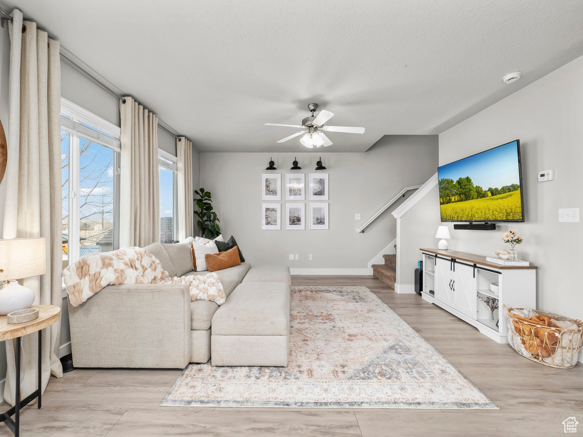 Living room featuring a ceiling fan, baseboards, light wood finished floors, and stairs