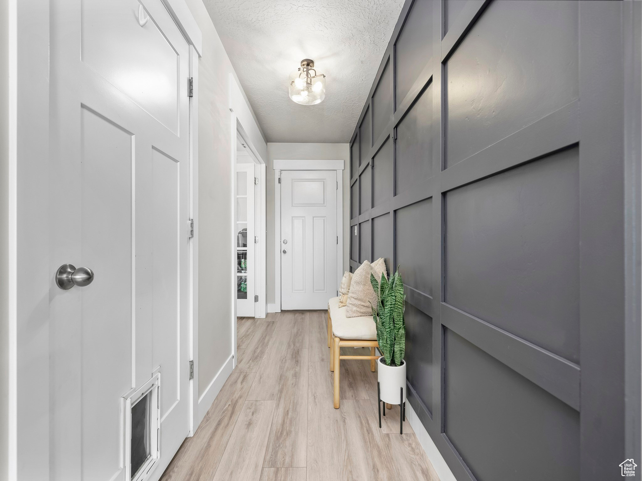 Corridor with light wood-type flooring, visible vents, a textured ceiling, and baseboards