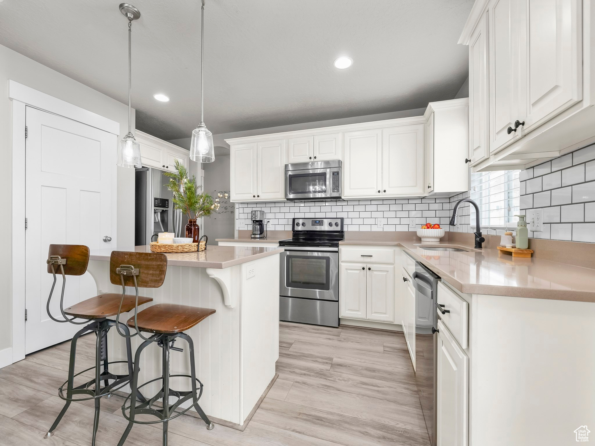 Kitchen featuring stainless steel appliances, a sink, white cabinetry, light countertops, and a center island