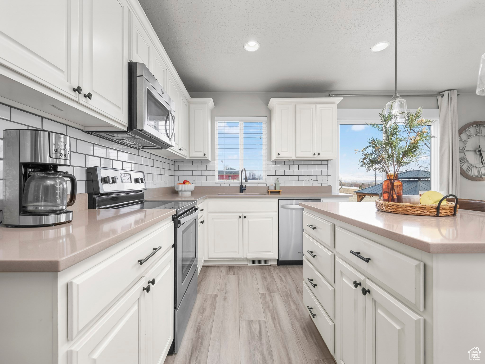 Kitchen with pendant lighting, light countertops, appliances with stainless steel finishes, white cabinetry, and a sink