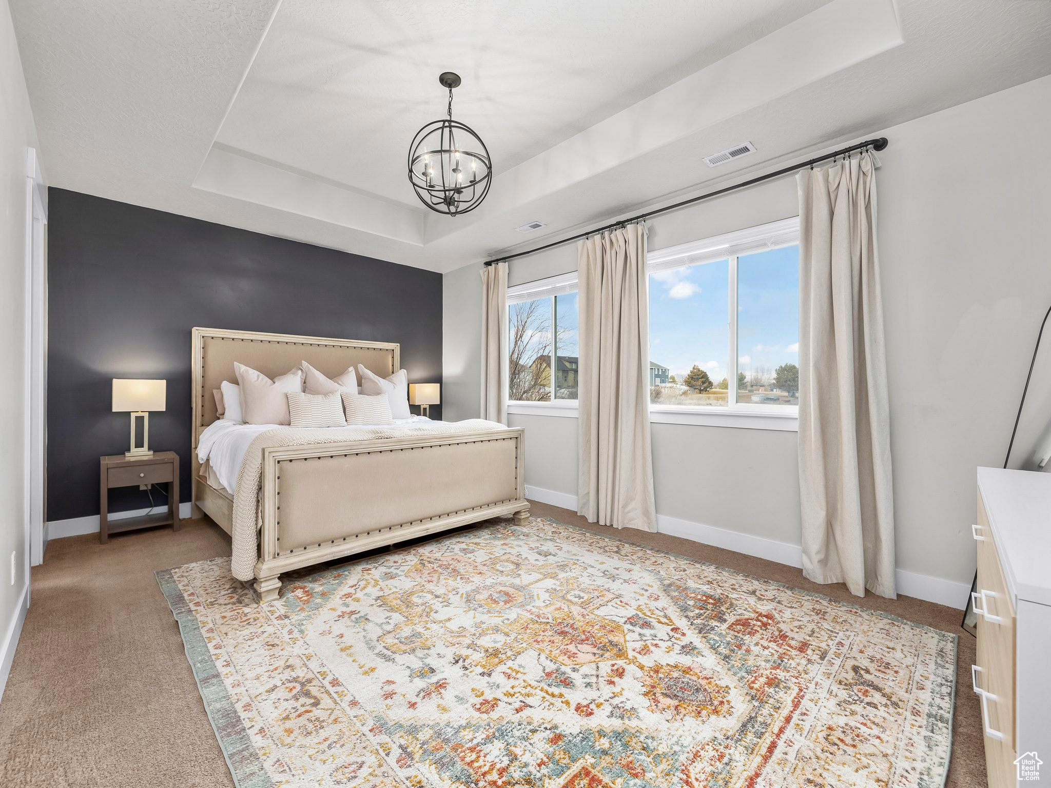 Bedroom featuring baseboards, visible vents, a tray ceiling, and a notable chandelier