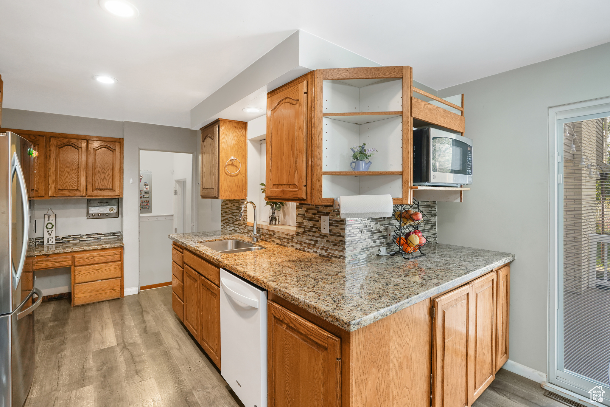 Kitchen with appliances with stainless steel finishes, brown cabinets, a sink, and light stone counters