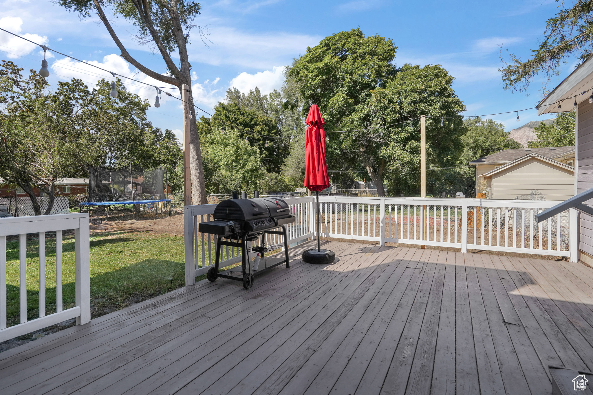 Wooden deck featuring a trampoline, grilling area, and a yard