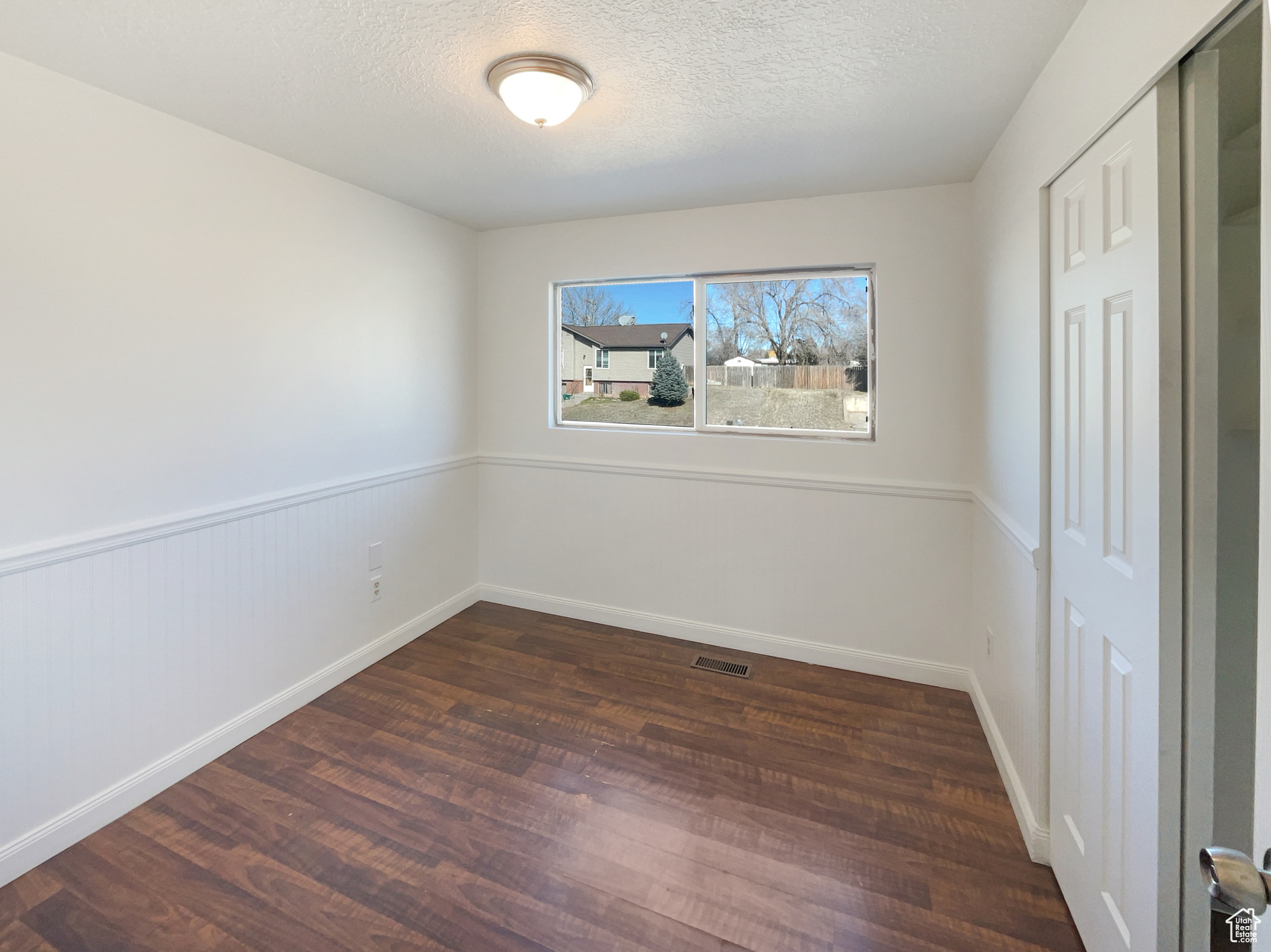Unfurnished room featuring visible vents, dark wood finished floors, a textured ceiling, and wainscoting