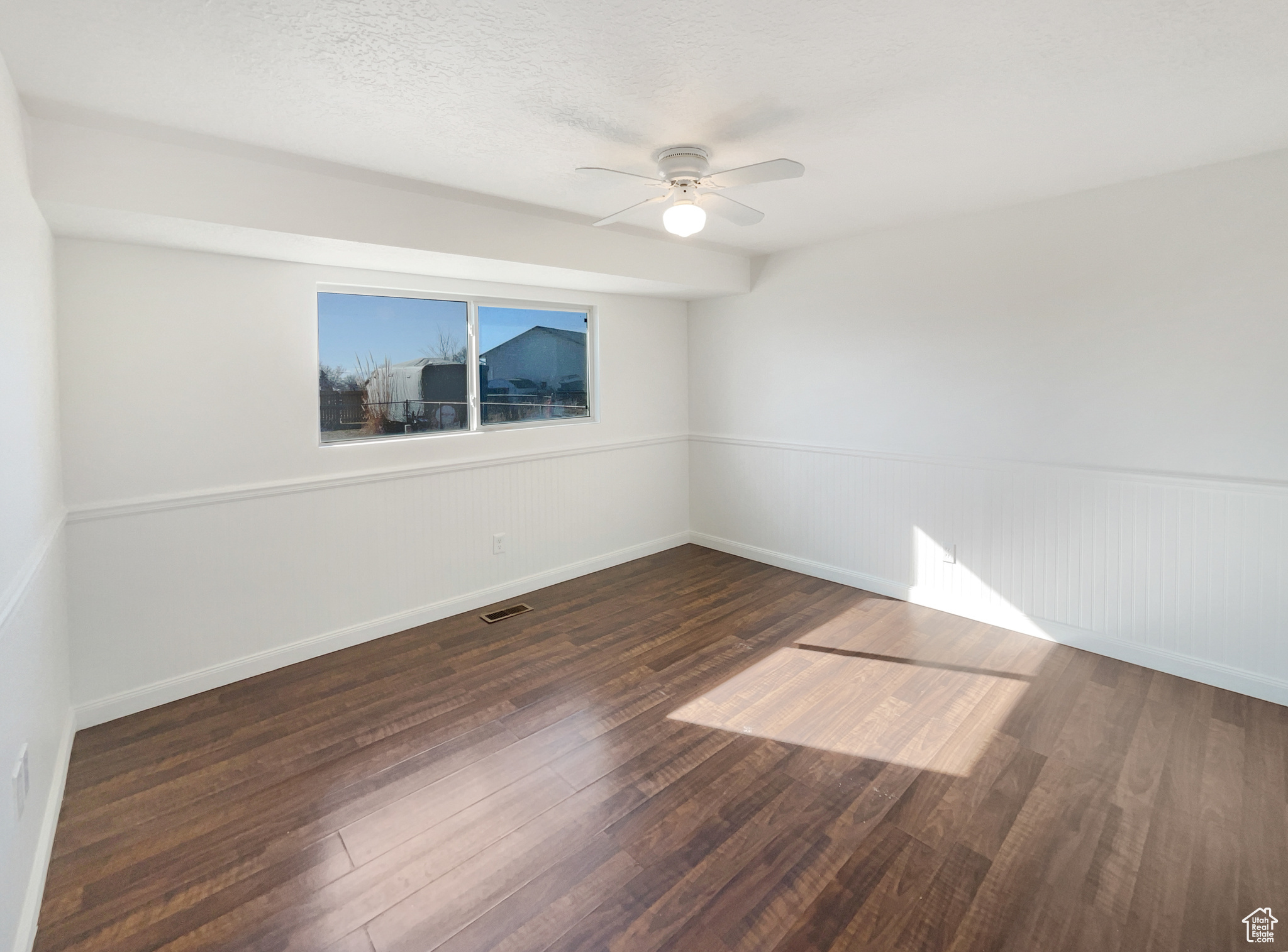 Empty room featuring a wainscoted wall, visible vents, dark wood-type flooring, a ceiling fan, and a textured ceiling