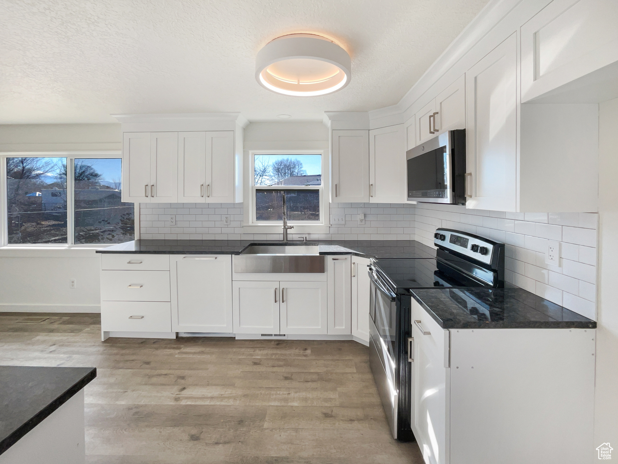 Kitchen with stainless steel appliances, backsplash, light wood-style floors, white cabinets, and a sink