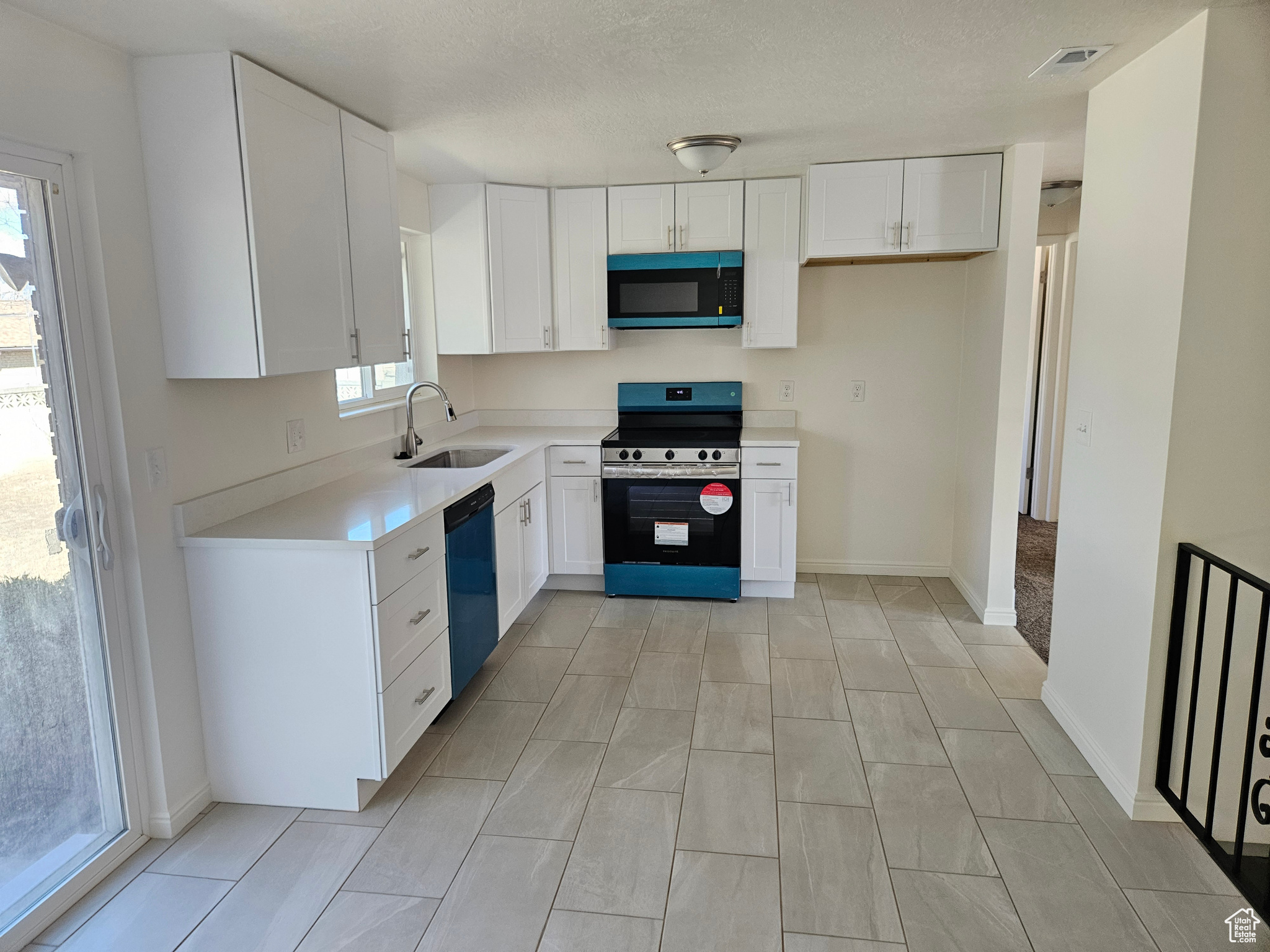 Kitchen featuring white cabinets, dishwasher, stainless steel electric stove, light countertops, and a sink