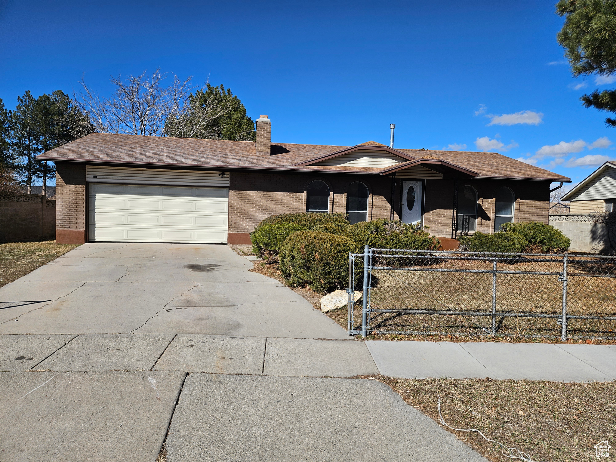 Ranch-style house with a garage, driveway, brick siding, and fence