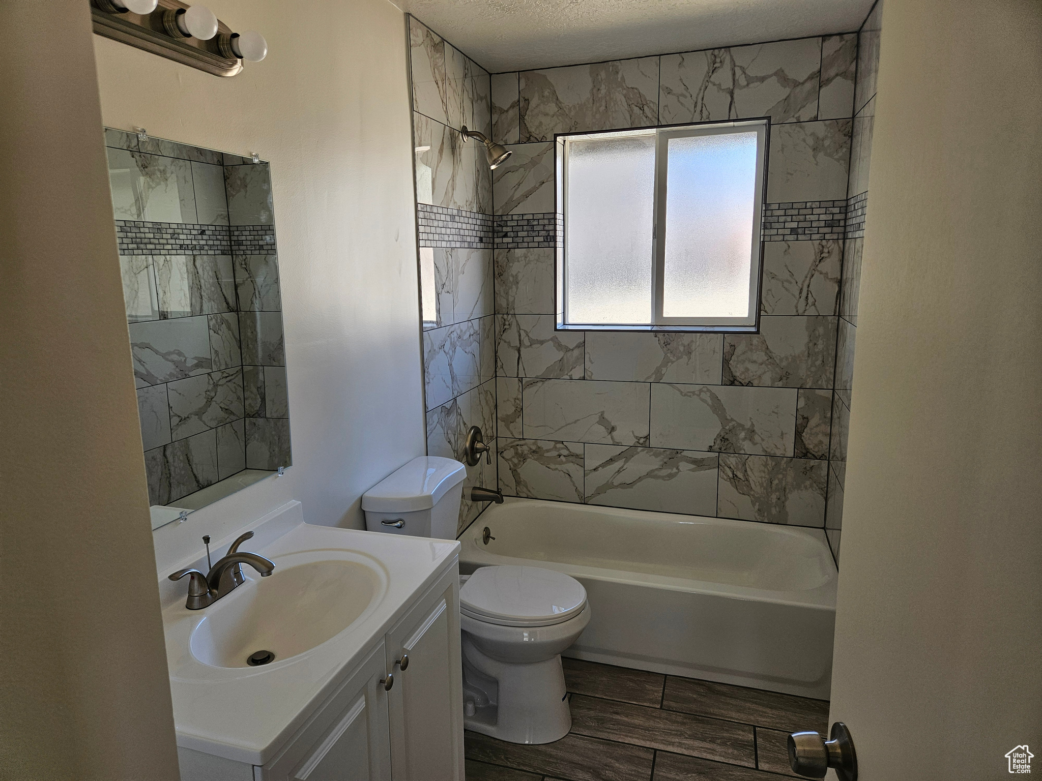 Bathroom featuring toilet, shower / tub combination, vanity, a textured ceiling, and wood finish floors