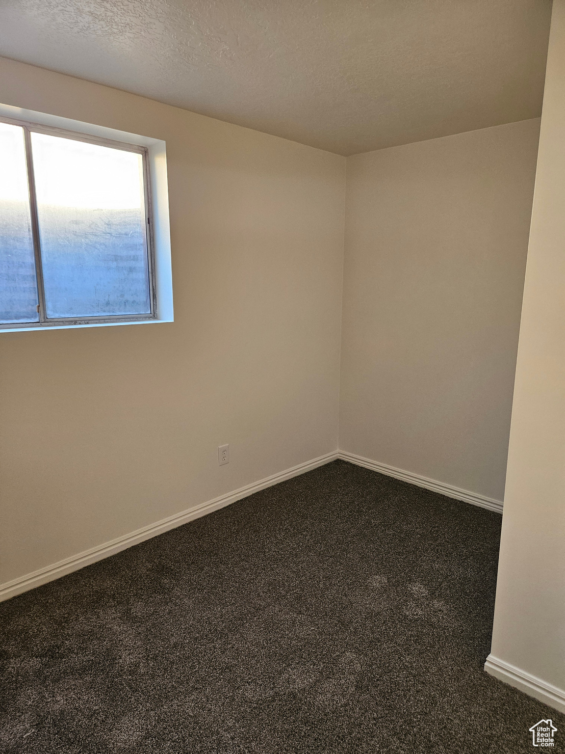 Unfurnished room with baseboards, dark carpet, and a textured ceiling