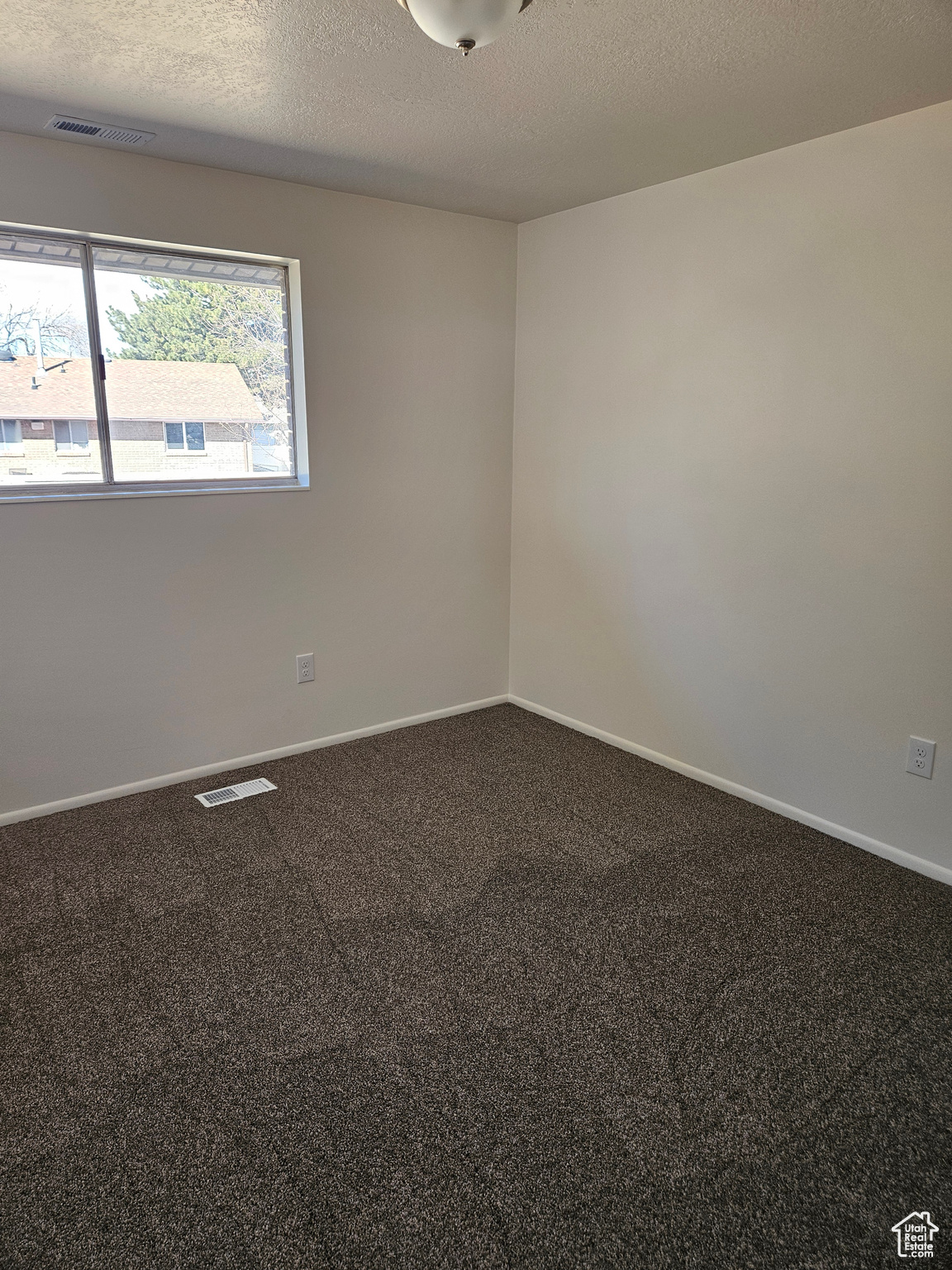 Empty room with a textured ceiling, carpet flooring, visible vents, and baseboards