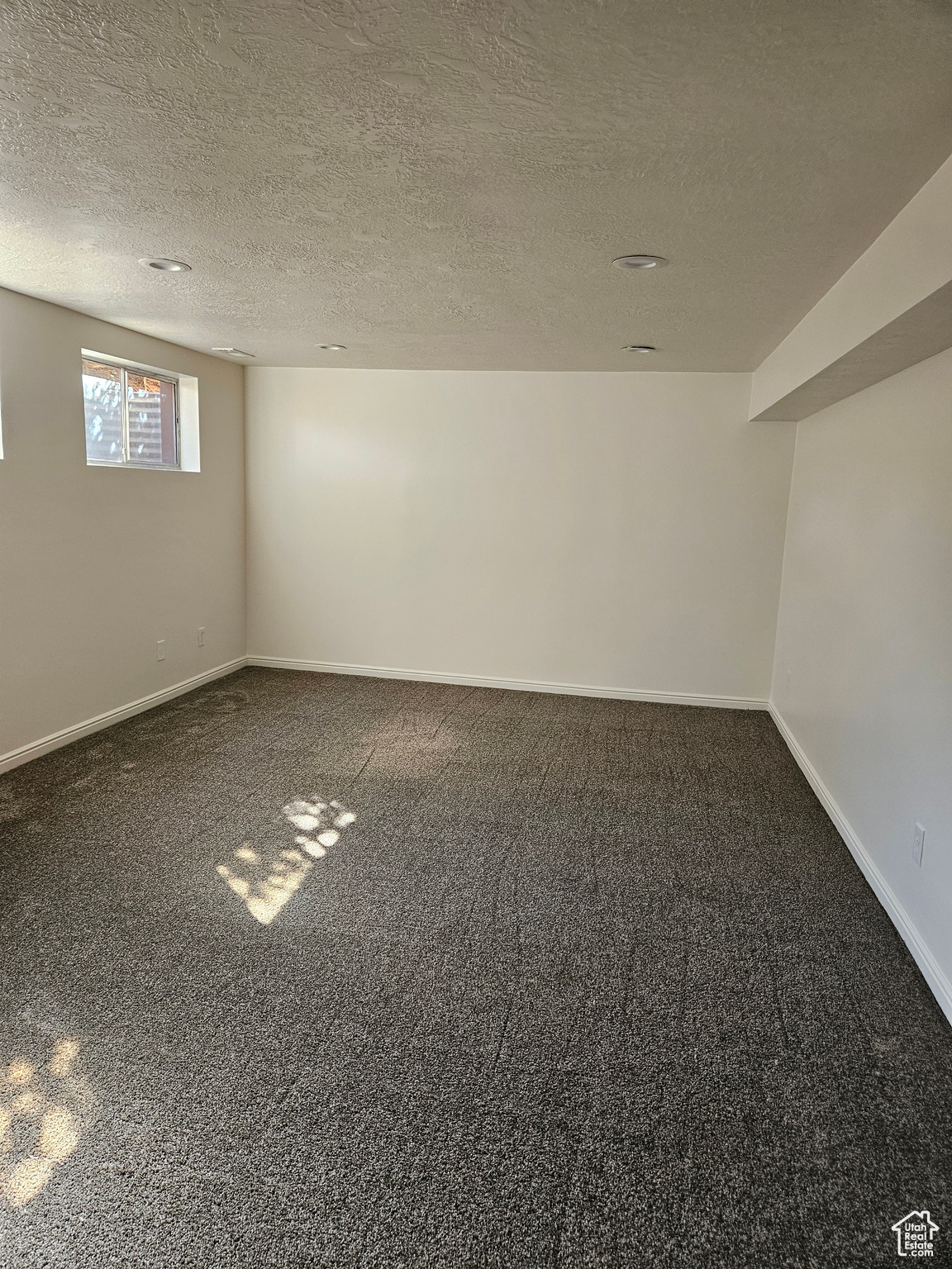 Spare room featuring baseboards, dark colored carpet, and a textured ceiling