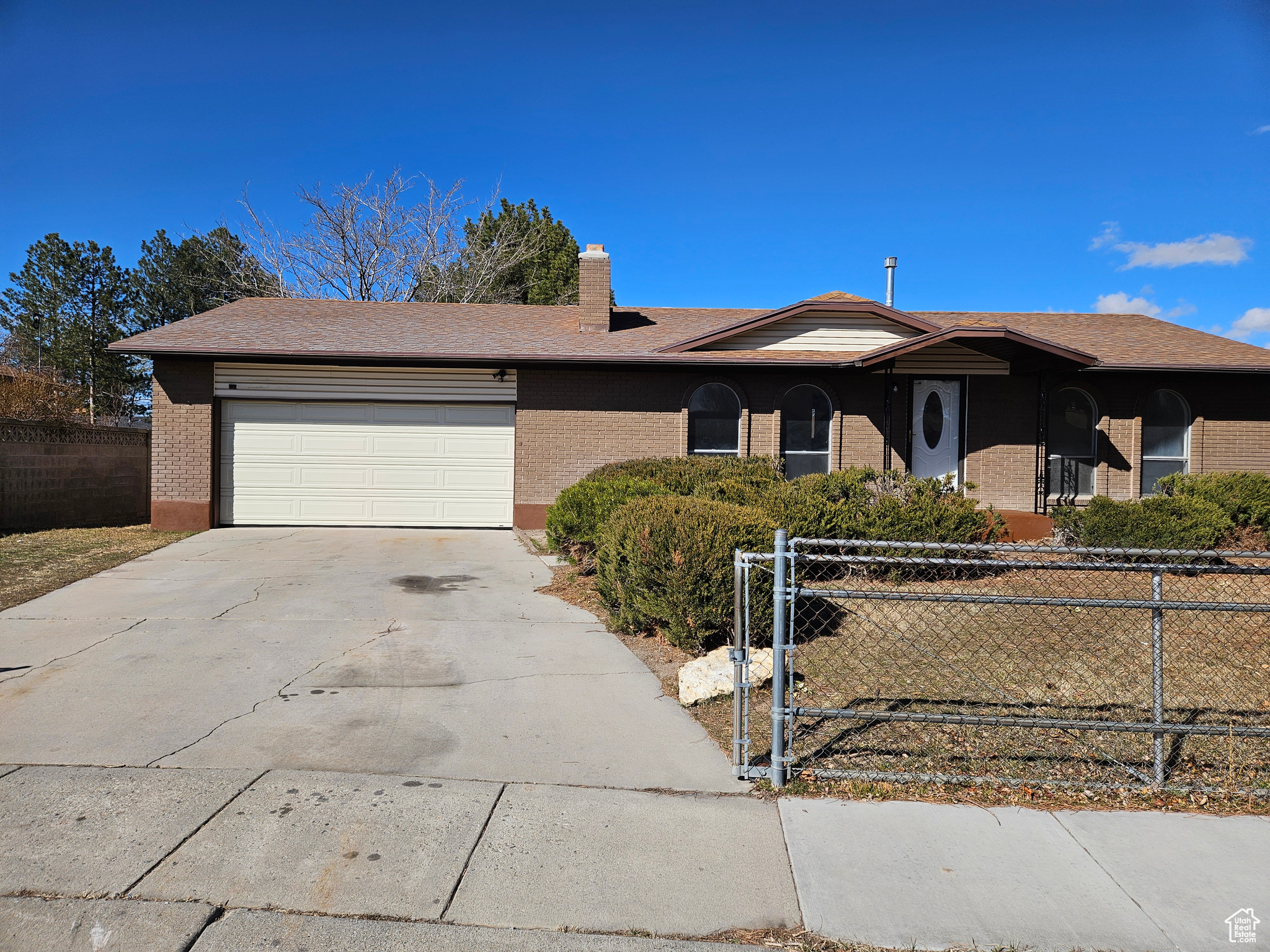 Ranch-style home with an attached garage, fence, concrete driveway, and brick siding