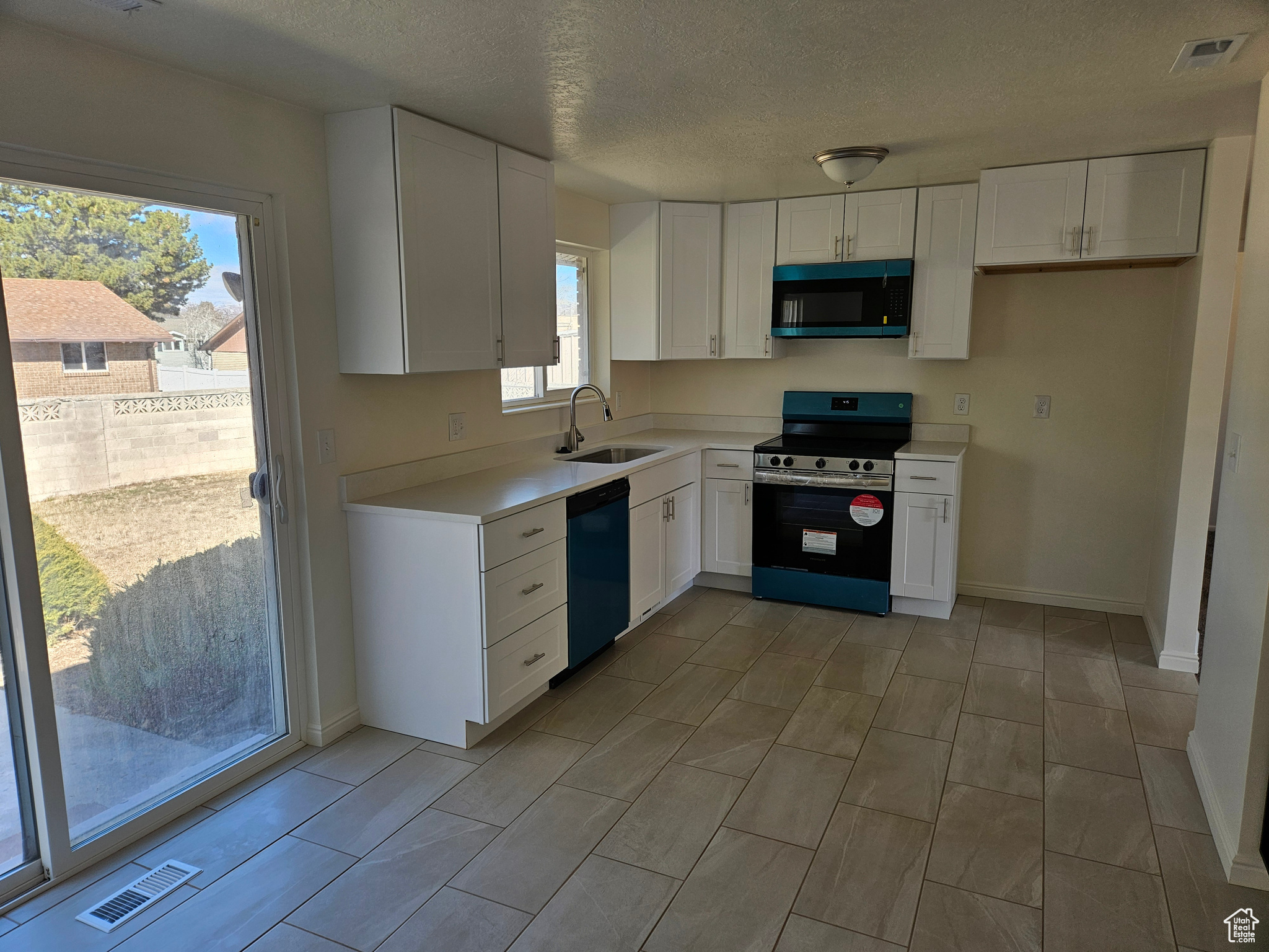 Kitchen with a sink, white cabinets, black dishwasher, light countertops, and stainless steel range with electric stovetop