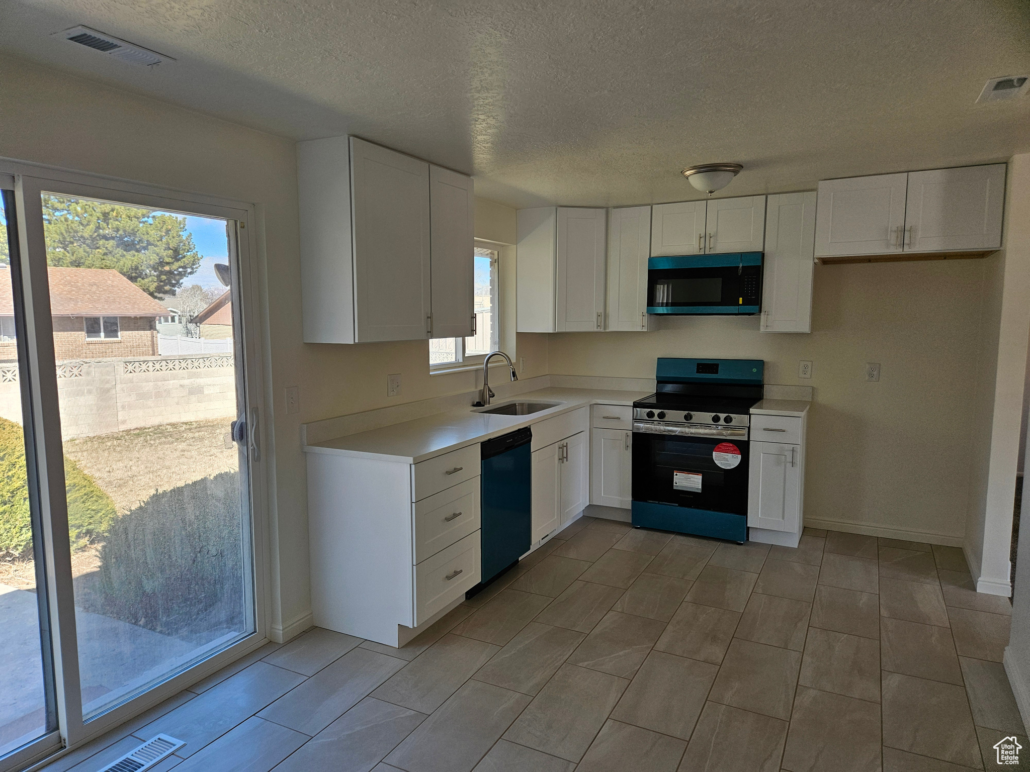 Kitchen featuring black dishwasher, light countertops, electric stove, and white cabinets