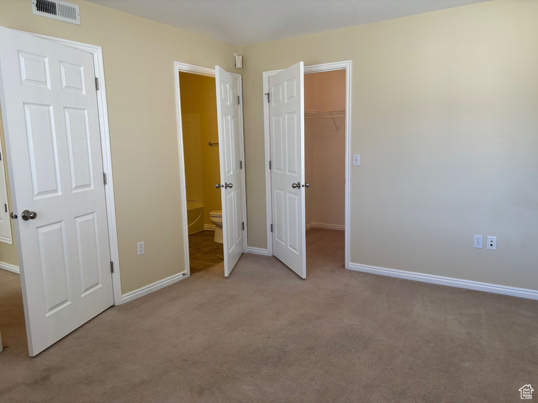 Master bedroom with light carpet, a walk in closet, and master bathroom