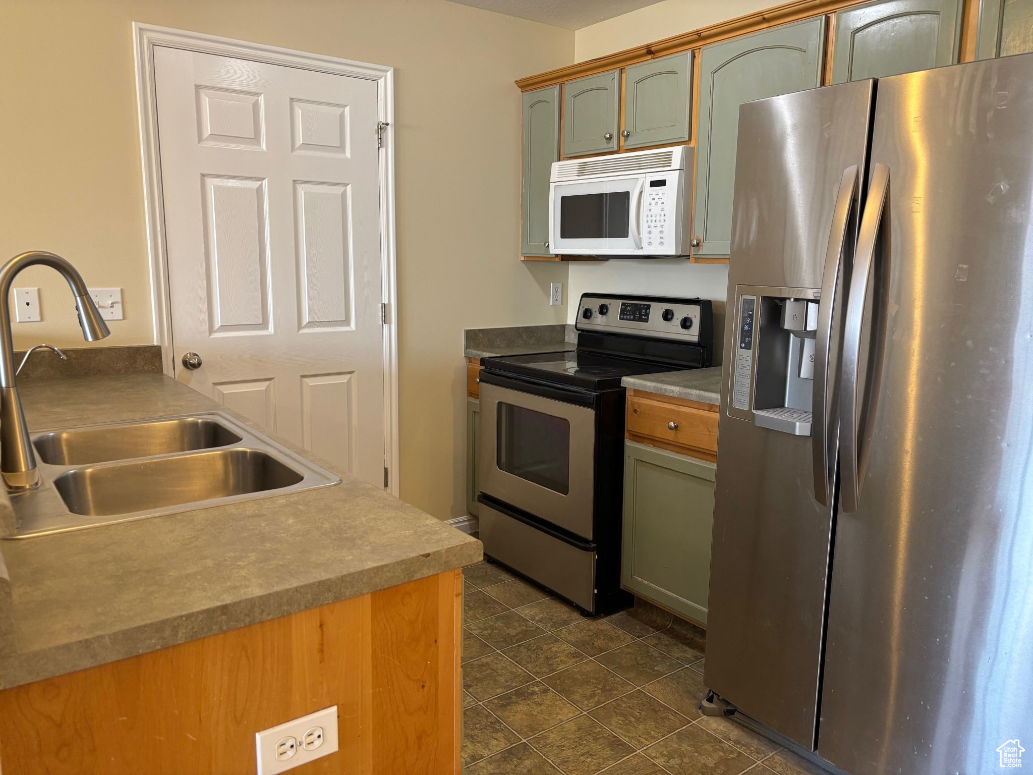 Kitchen with appliances with stainless steel finishes, a sink, and green cabinets