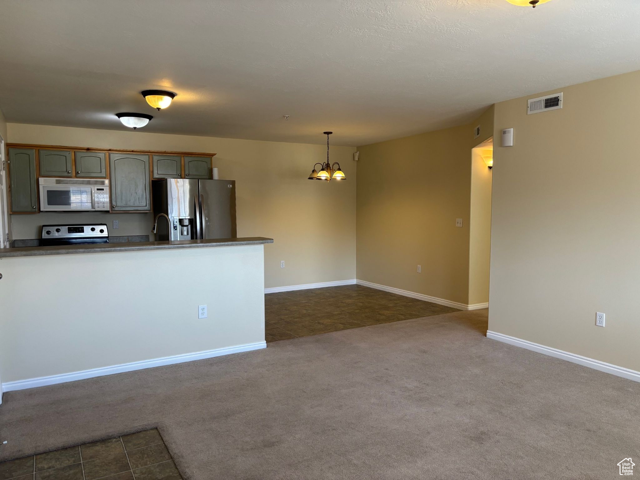 Kitchen with visible vents, hanging light fixtures, appliances with stainless steel finishes, dark carpet, and dark countertops
